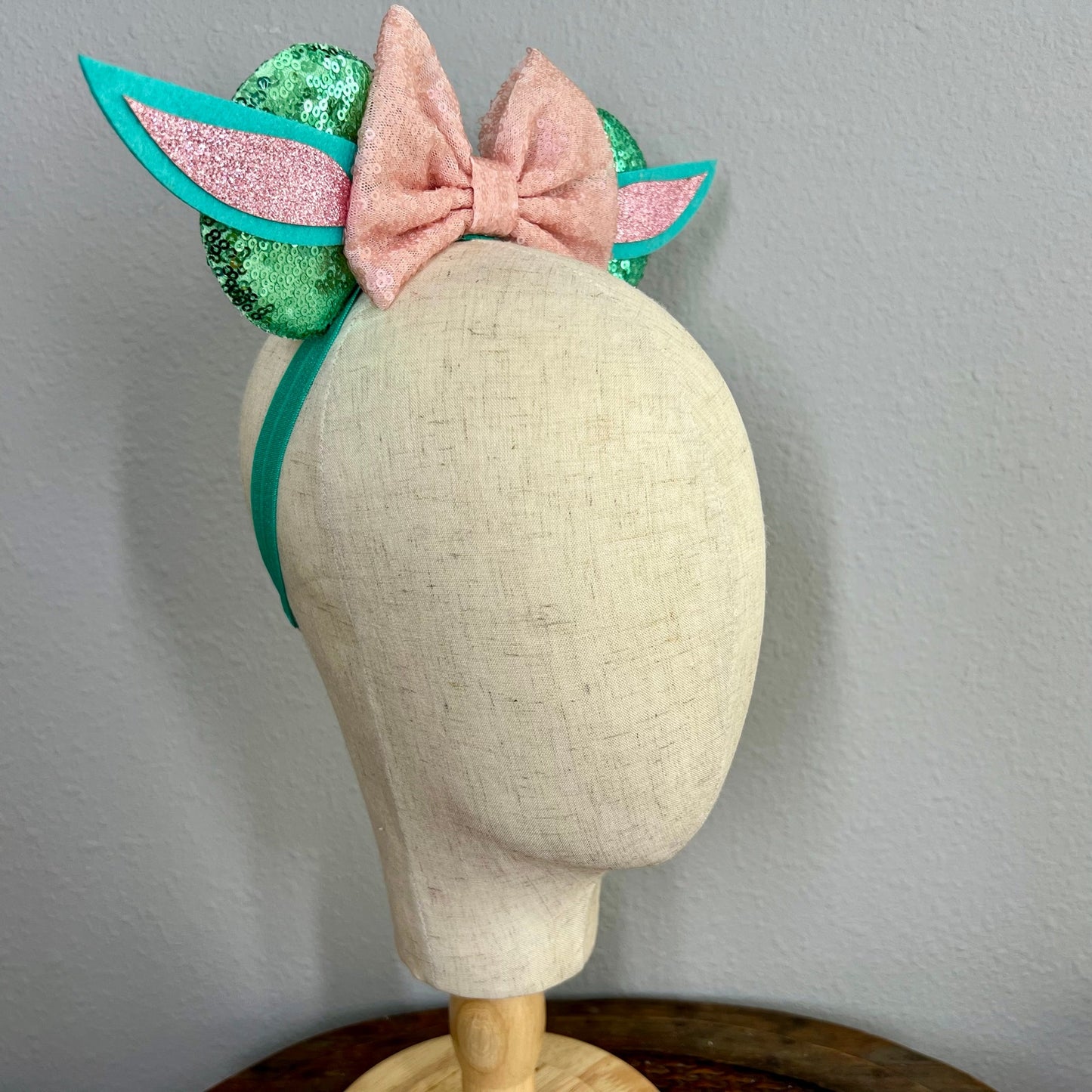 Headband with pink bow and green glittery accents on a mannequin head against a gray background