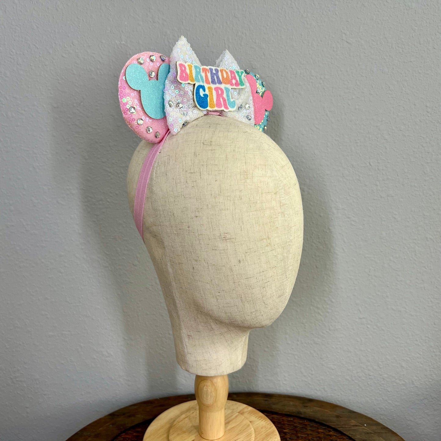Pink and blue elastic mouse ears headband with glitter 'birthday girl' centerpiece on a mannequin head