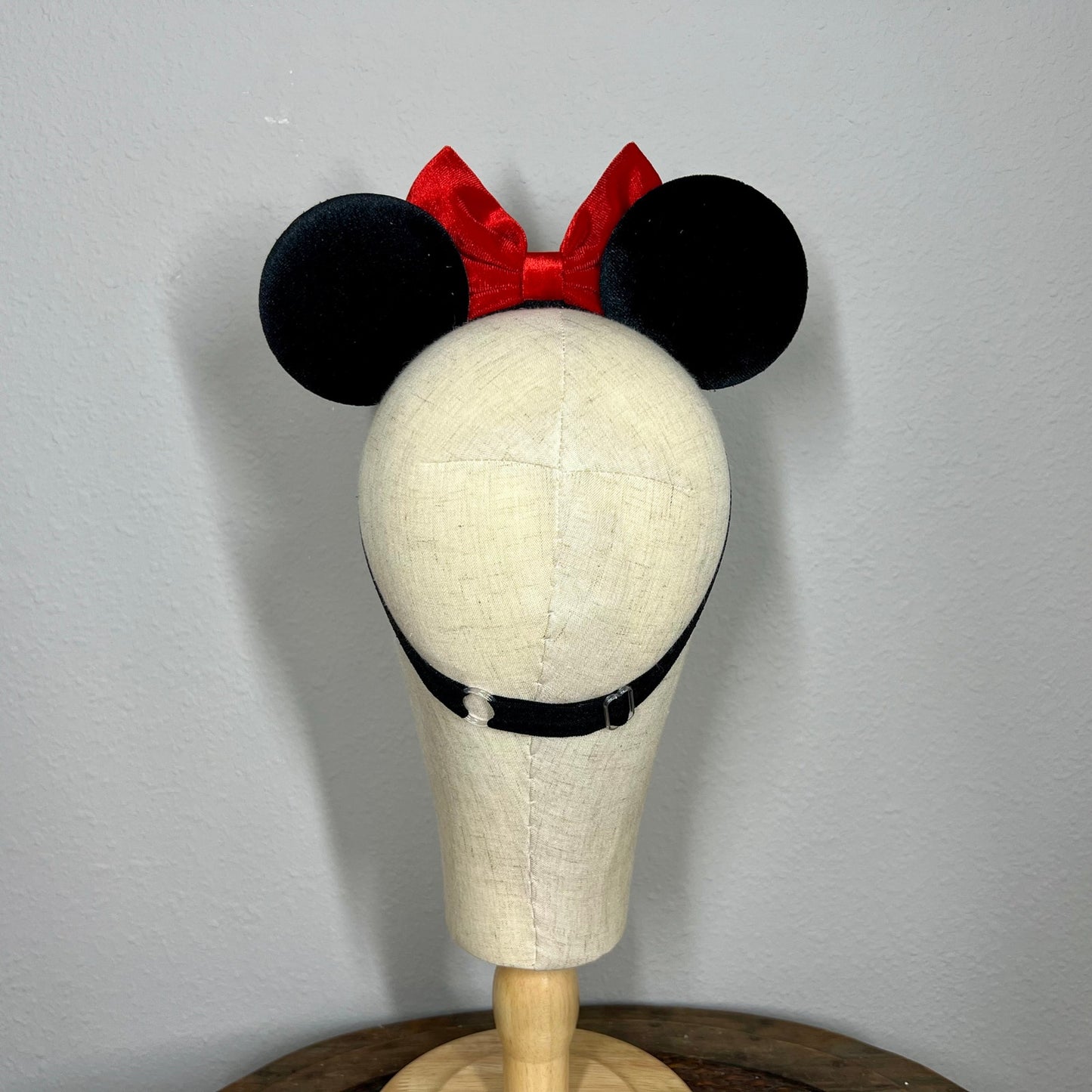 Mannequin head wearing black and red mouse ears with a red bow on a plain background