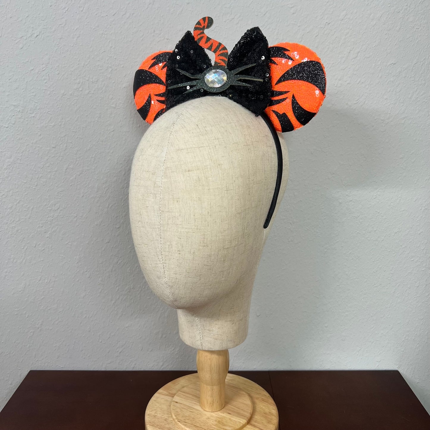 Orange mouse ears with black sequin bow, with black tiger stripes, black glitter whiskers, rhinestone nose, and orange and black tiger tail centerpiece on a mannequin head