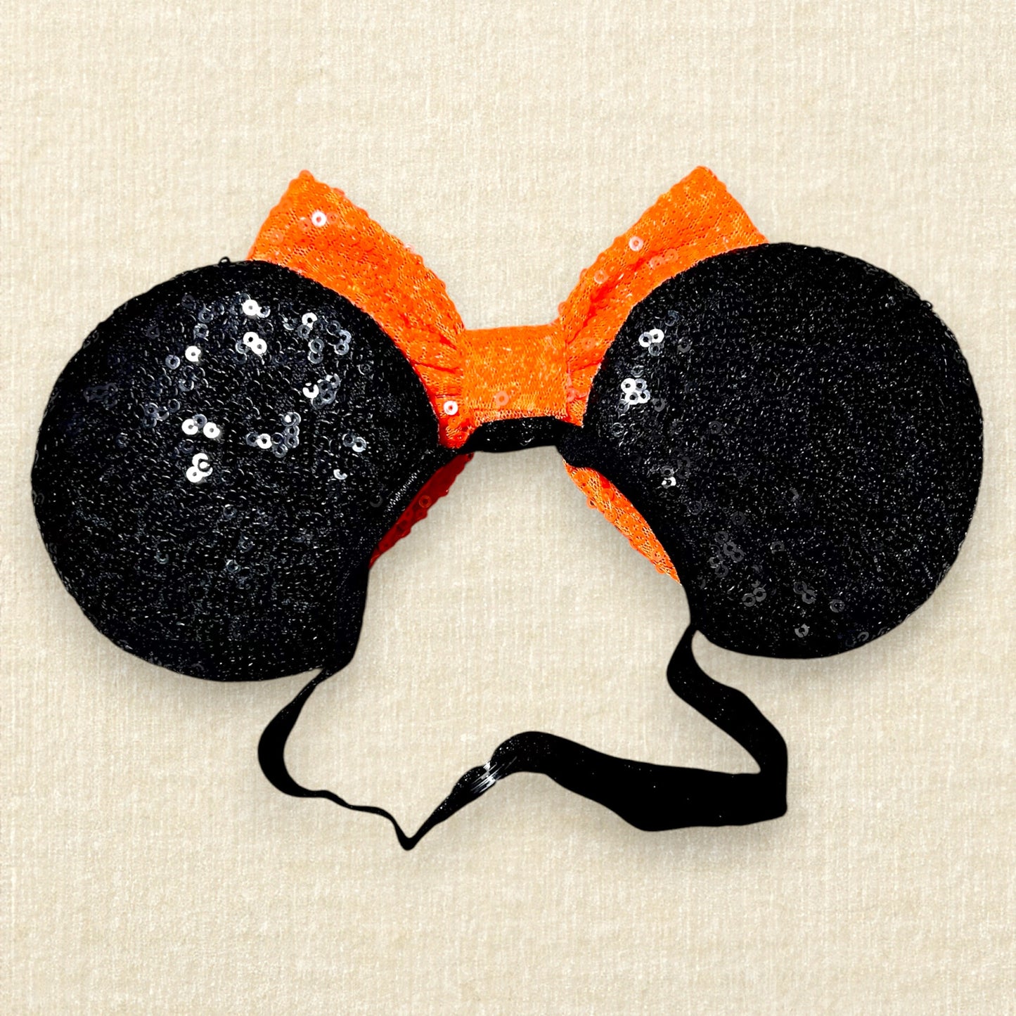 Black sequin Halloween-themed mouse ears with candy corn pieces, rhinestones, and an orange bow on an elastic headband (back view)