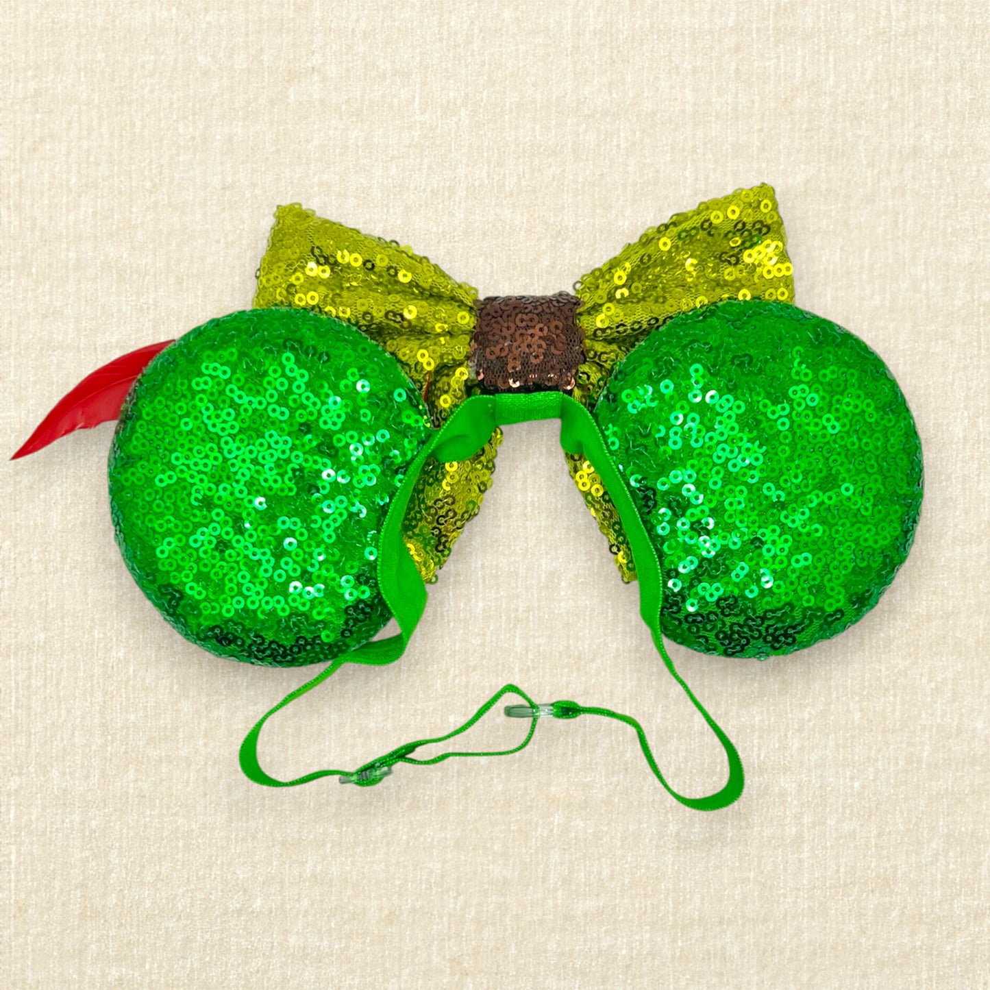 Green sequin mouse ears with lighter green sequin bow and red feather on an elastic headband (back view)