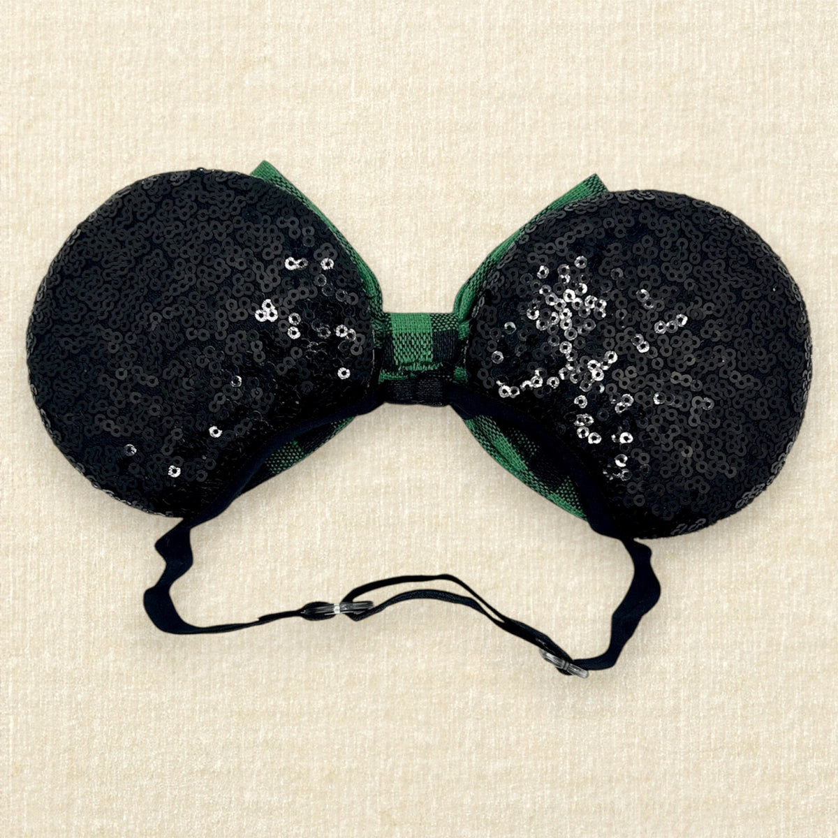 A festive Christmas-themed mouse ears headband with black sequin ears and a green and black buffalo plaid bow on an elastic headband (back view)
