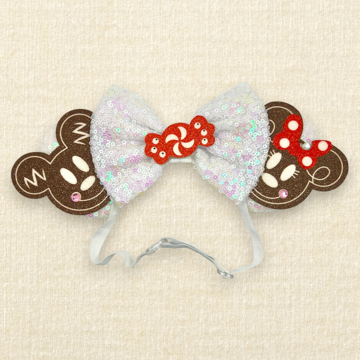 Holiday-themed mouse ears headband with iridescent white ears and bow, gingerbread mouse cookies, and red and white peppermint candy centerpiece on an elastic headband