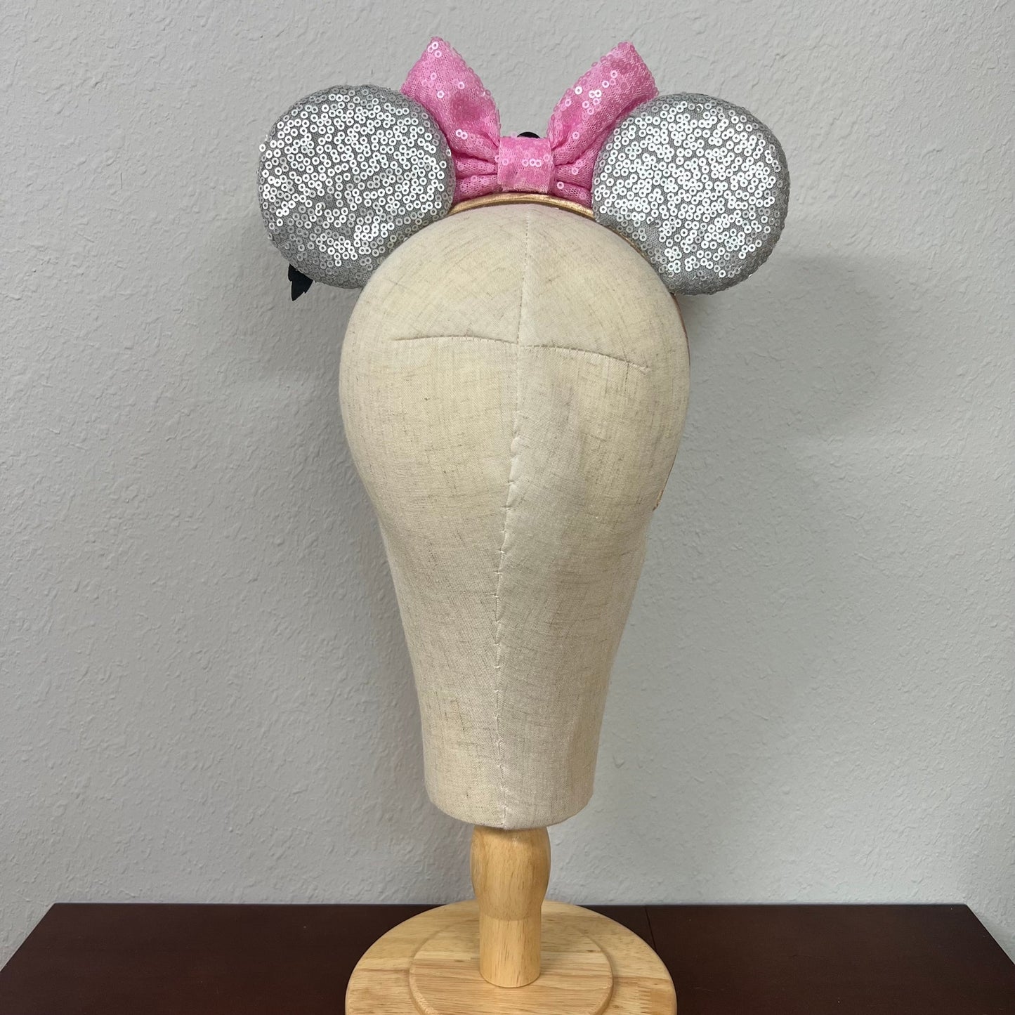 Mannequin head wearing silver and pink sequin mouse ears against a plain background