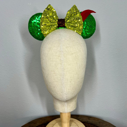 Green sequin elastic mouse ears with lighter green sequin bow and red feather headband on a mannequin with a gray background