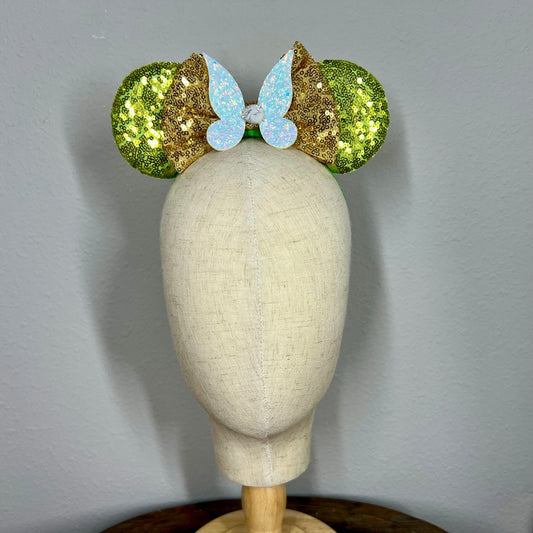 Green sequin mouse ears headband with gold bow and glitter fairy wings on a mannequin