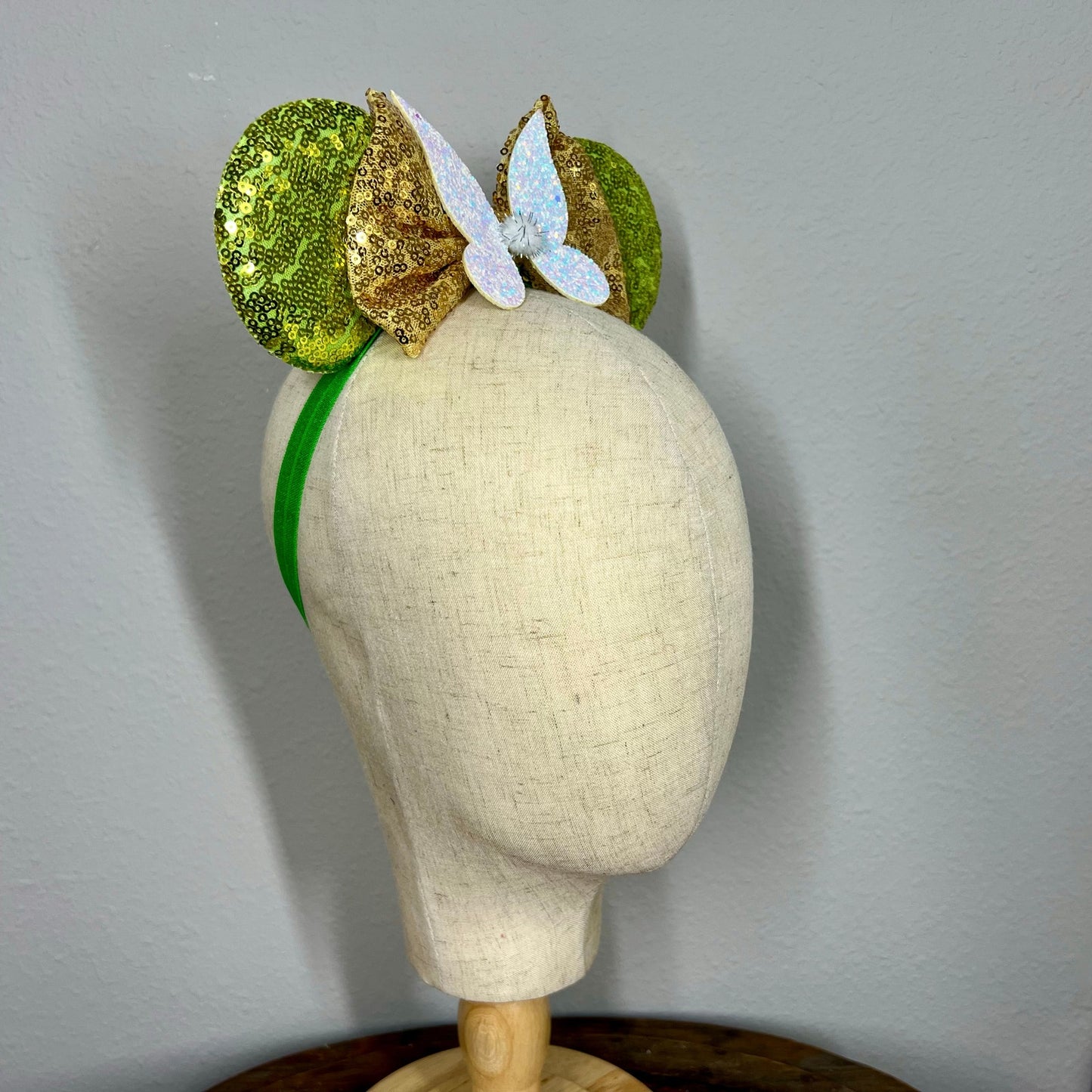 Green sequin mouse ears headband with gold bow and glitter fairy wings on a mannequin