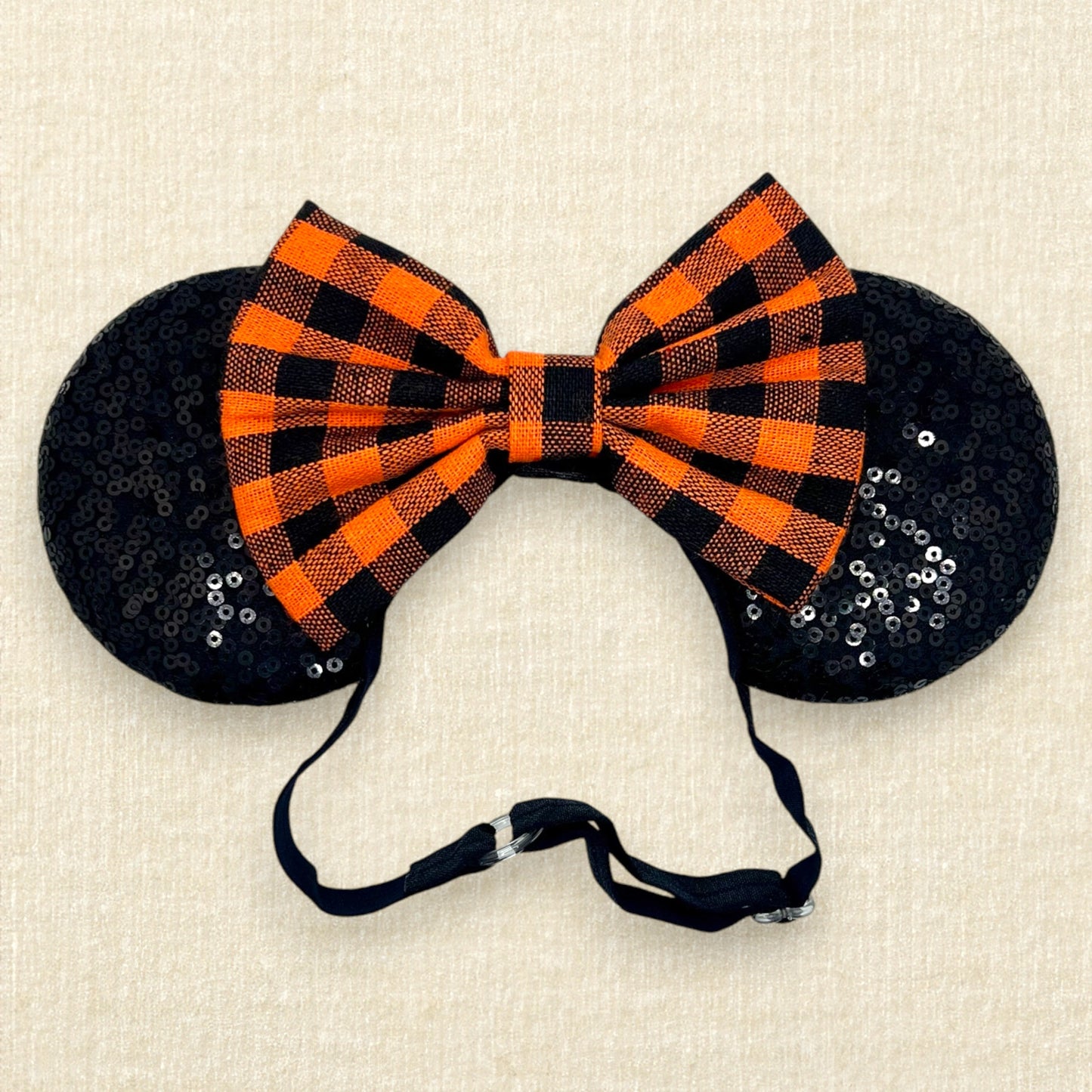 Fall-themed mouse ears with black ears and orange and black buffalo plaid bow on an elastic headband