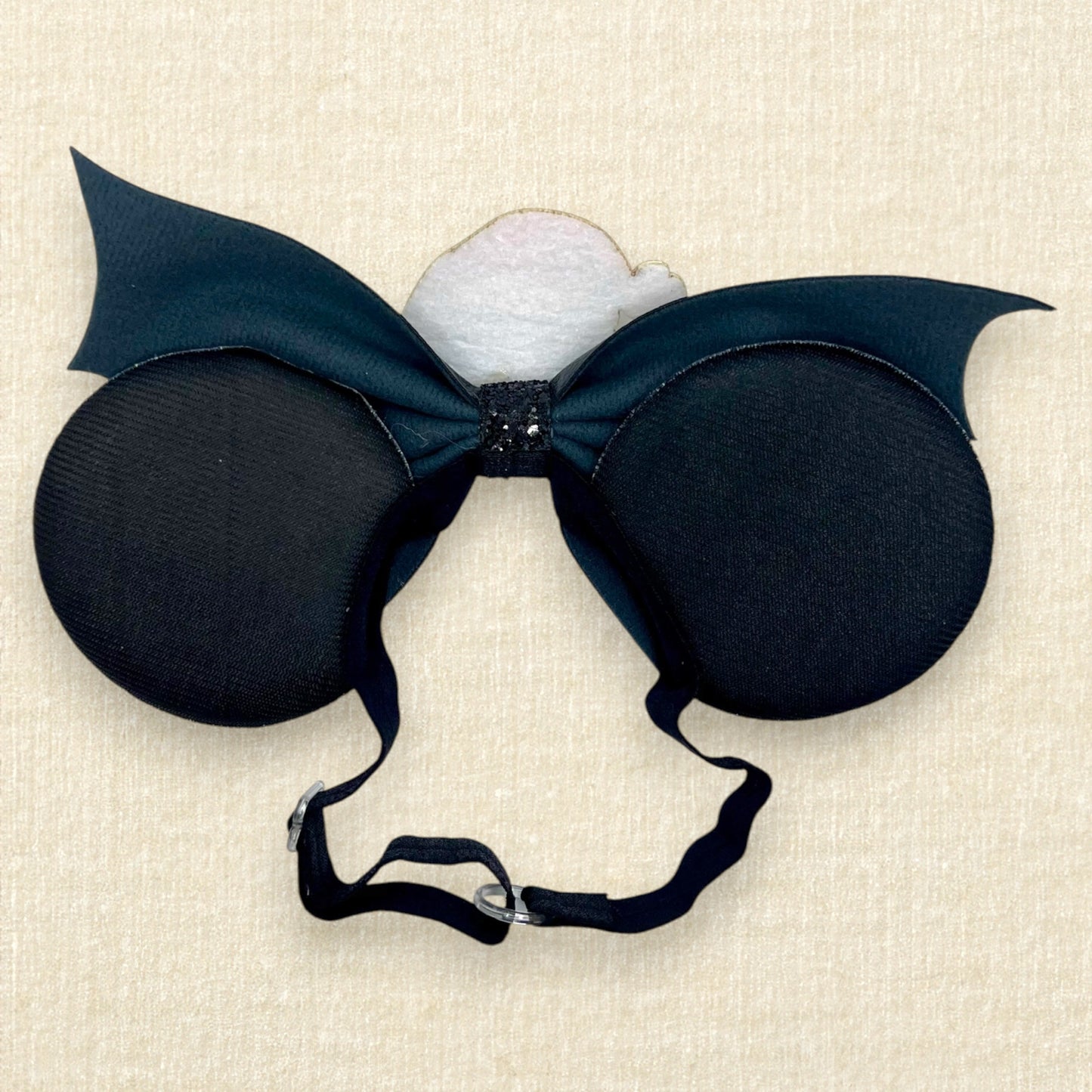 Halloween-themed mouse ears with black and white fabric ears, black faux leather bat wing bow, and glitter Sandy Claws centerpiece on an elastic headband (back view)