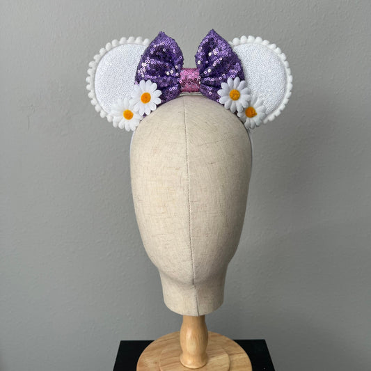 Mouse ears headband with purple sequin bow and white floral design on a mannequin head against a gray background
