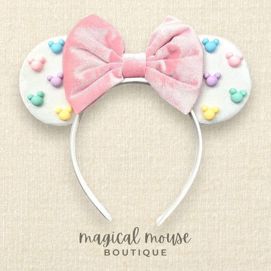 White mouse ears with a pink bow and pastel mouse-shaped pearls on a beige background, branded 'magical mouse boutique'.