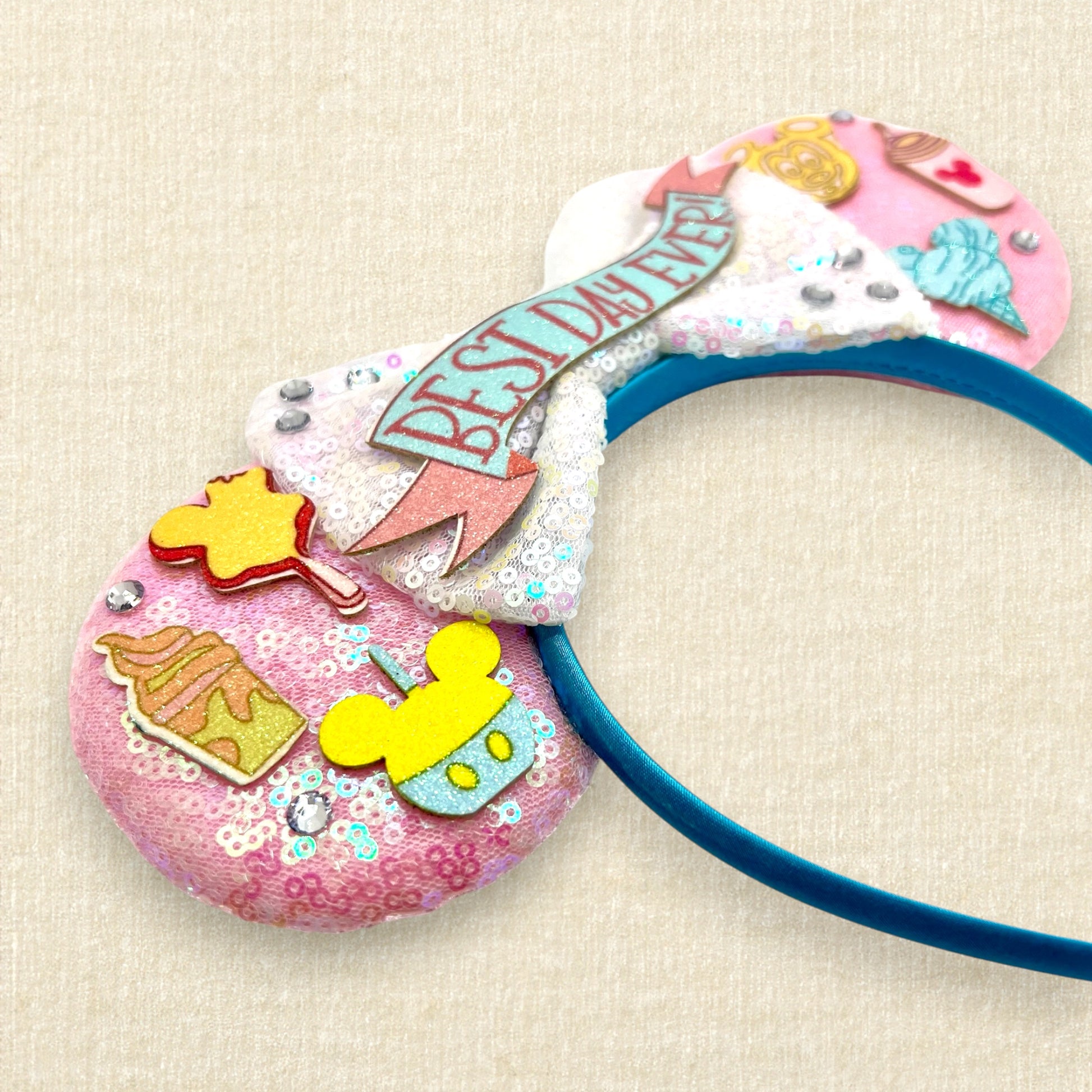 Pink mouse ears headband with glitter theme park snack details, iridescent white bow, and glitter "Best Day Ever!" text