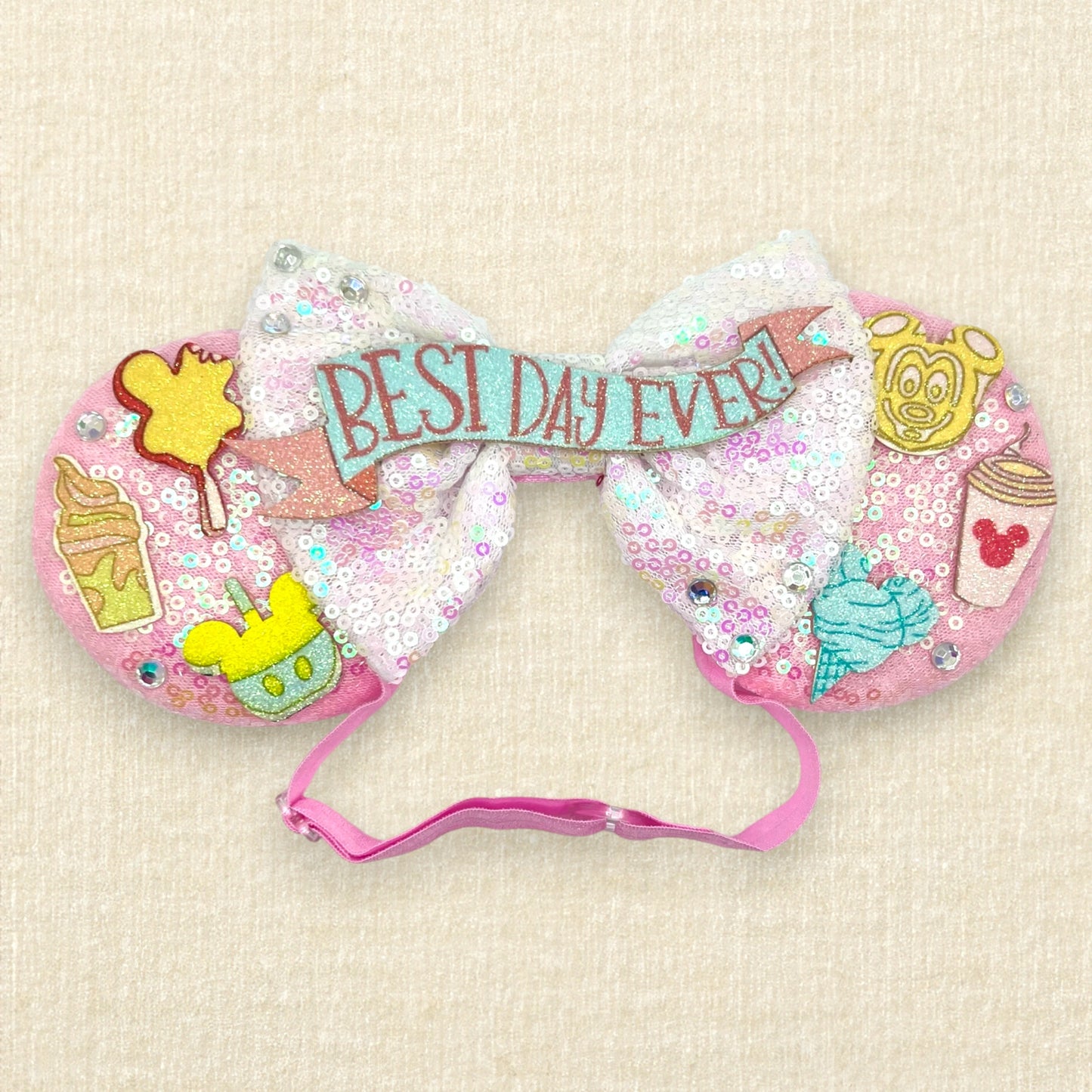 Pink mouse ears with glitter theme park treats, iridescent white bow, and glitter "Best Day Ever!" text on an elastic headband