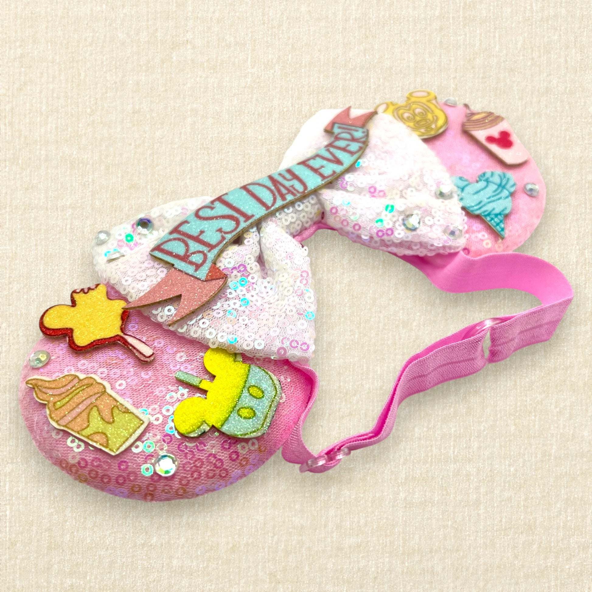 Pink mouse ears with glitter theme park treats, iridescent white bow, and glitter "Best Day Ever!" text on an elastic headband