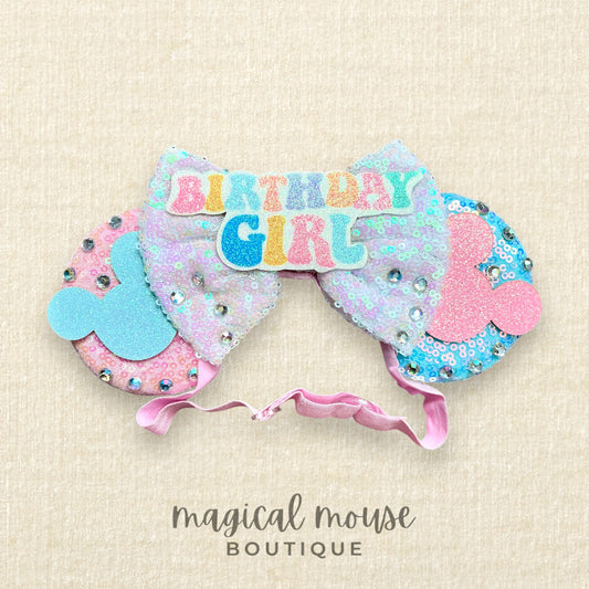 Pink and blue elastic mouse ears headband with 'Birthday Girl' text centerpiece on a beige background with 'magical mouse boutique' branding