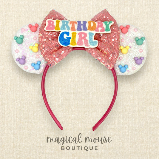 White sequin headband with pink bow, rainbow mouse-shaped pearls, and glitter "Birthday Girl" text centerpiece