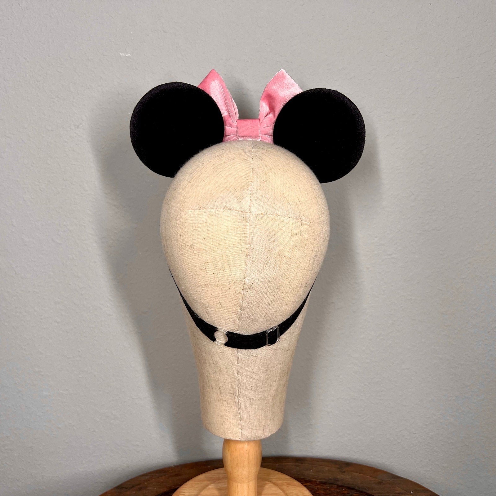 Mannequin head with black mouse ears and pink bow on a gray background