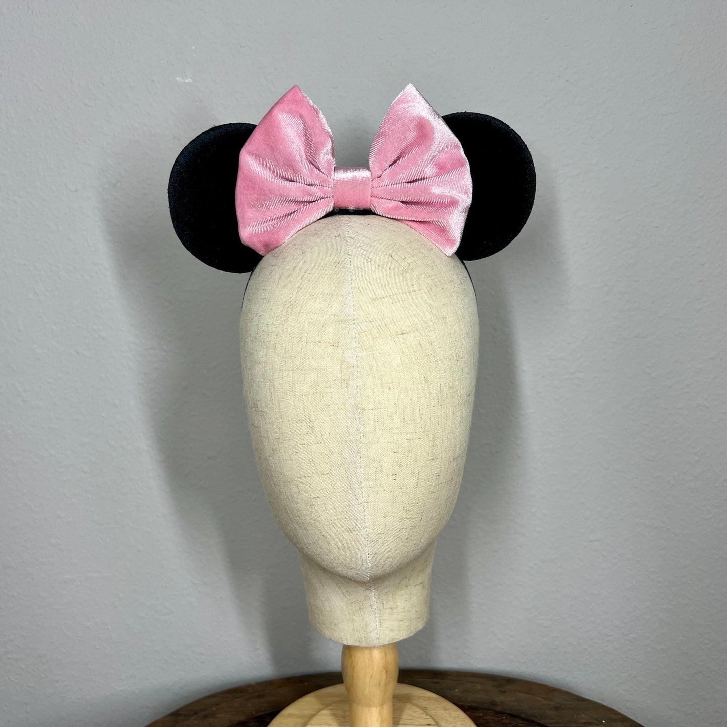 Black mouse ears with a pink bow on a mannequin head against a gray background