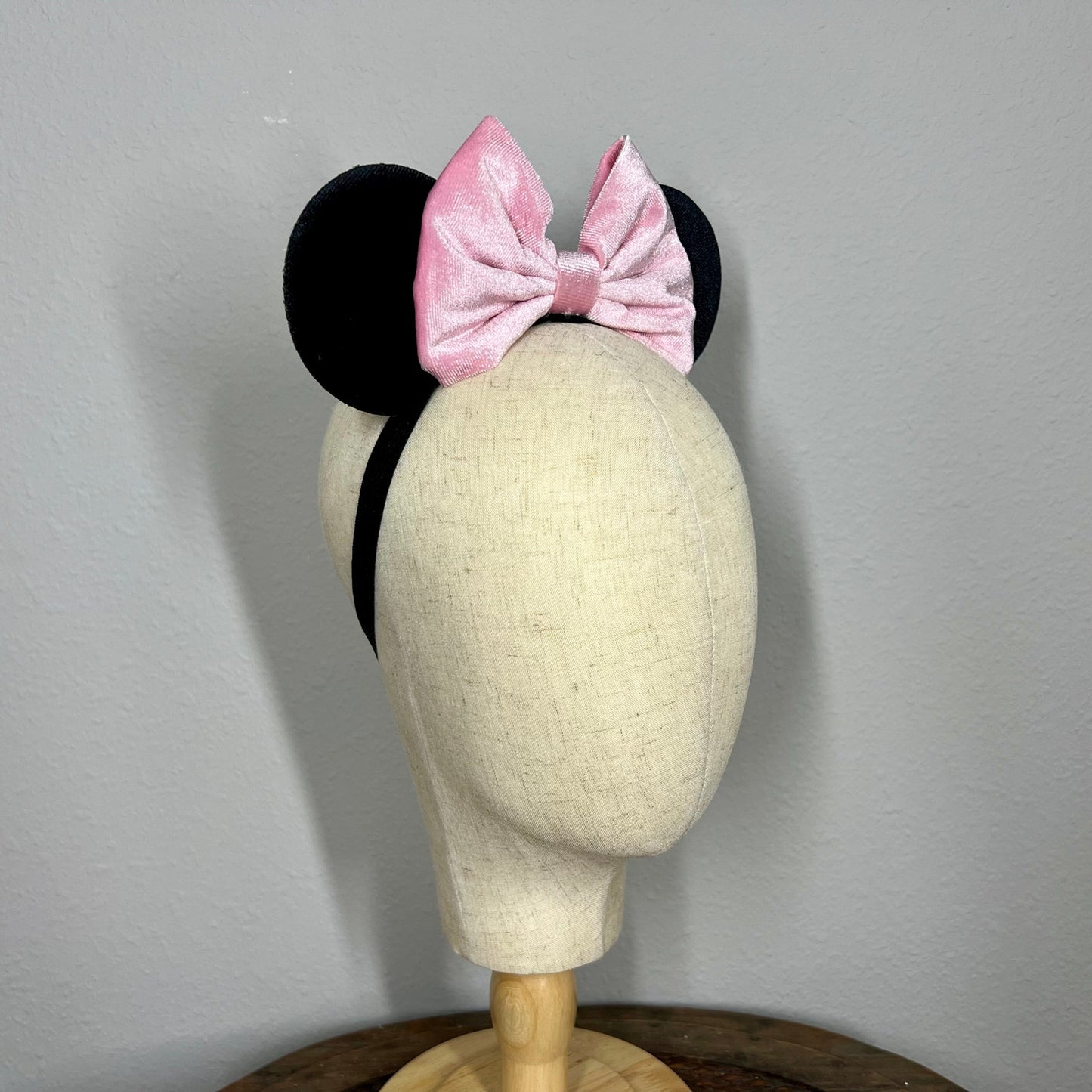 Black mouse ears with a pink bow on a mannequin head against a gray background