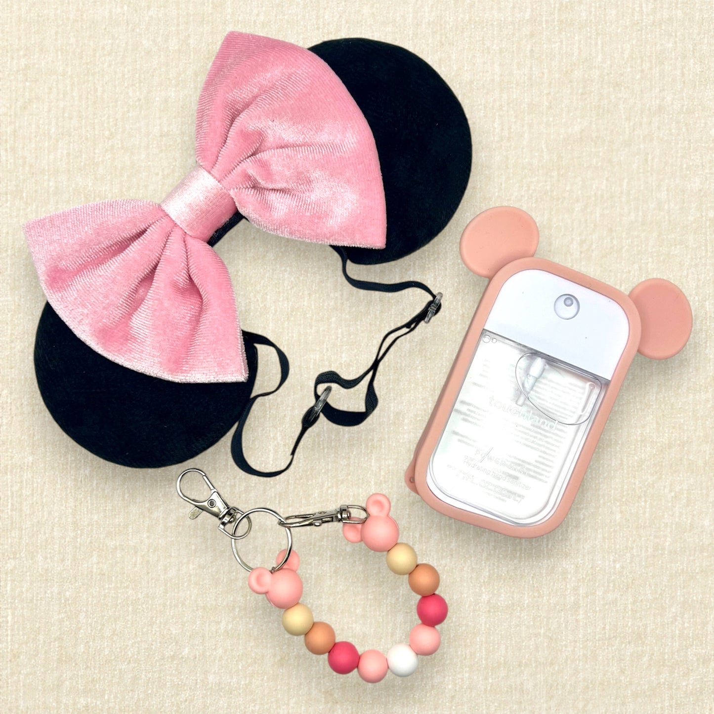Black velvet mouse ears with pink velvet bow on an elastic headband; spray hand sanitizer in a pink mouse ears case; pink beaded mouse ears holder clip