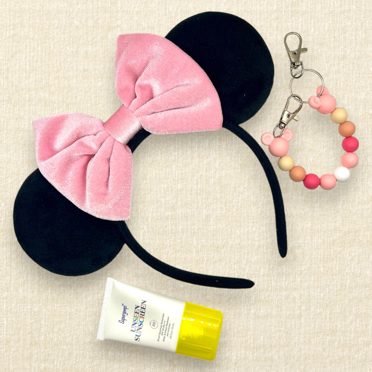 Black velvet mouse ears headband with pink velvet bow; tube of sunscreen; pink and white beaded mouse ears holder clip