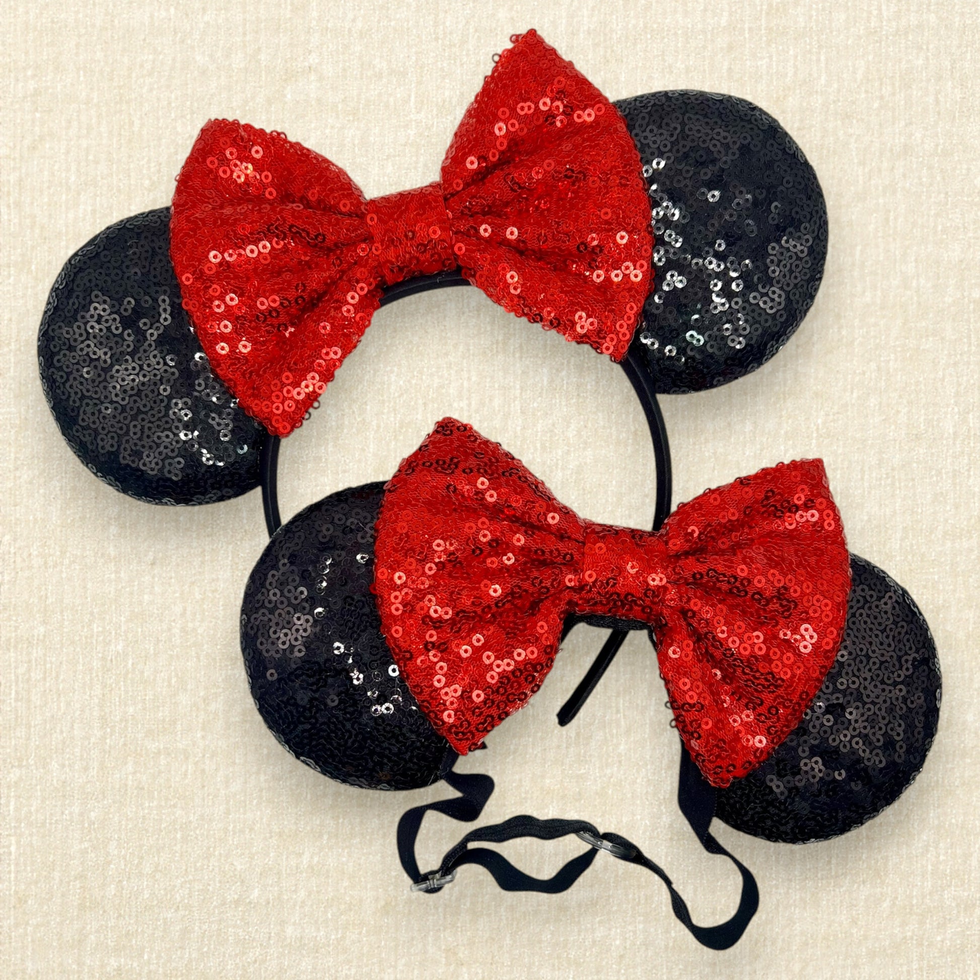 Two pairs of mouse ears with black sequin ears and red sequin bow, one on a standard headband and one with an elastic headband