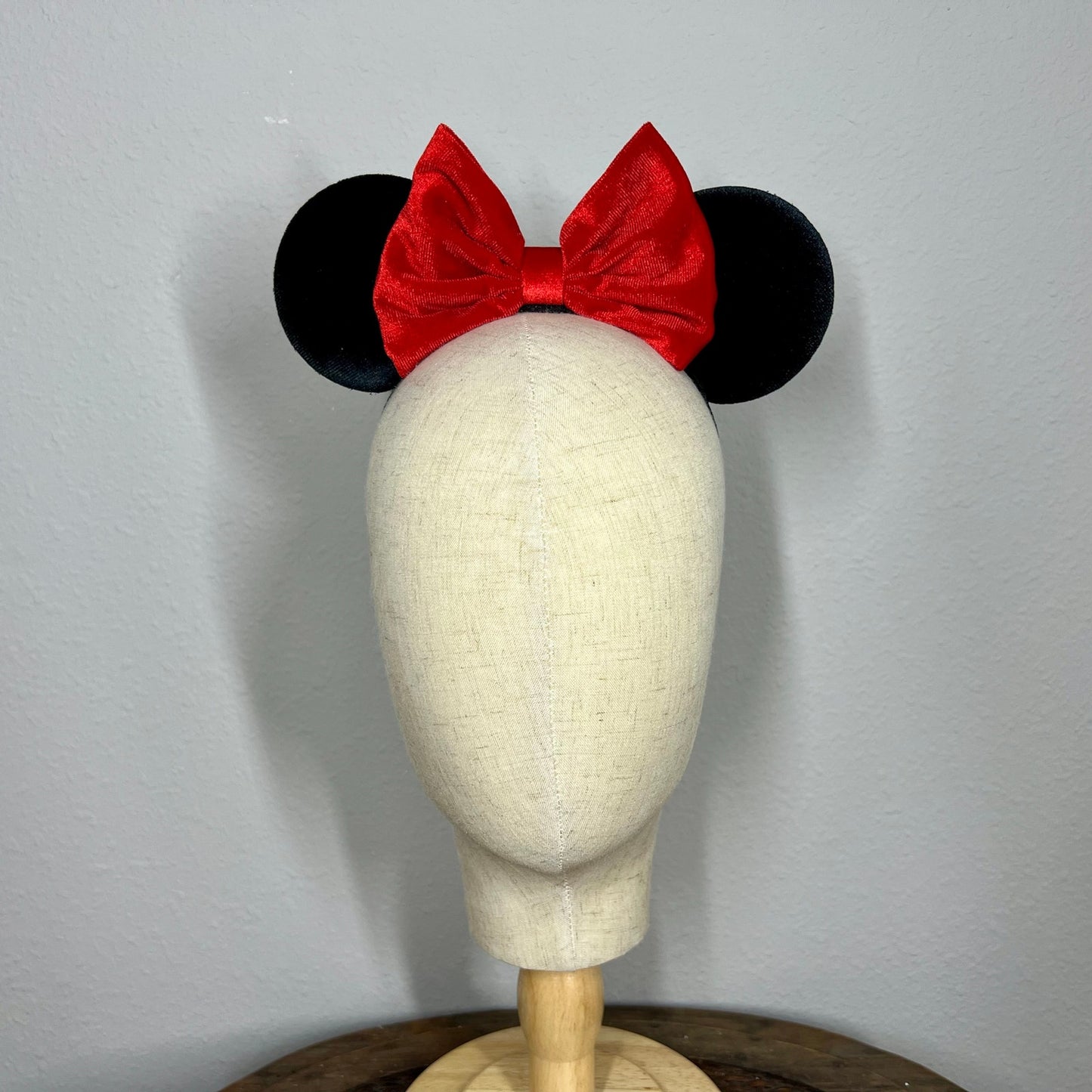 Black mouse ears with a red bow on a mannequin head against a gray background
