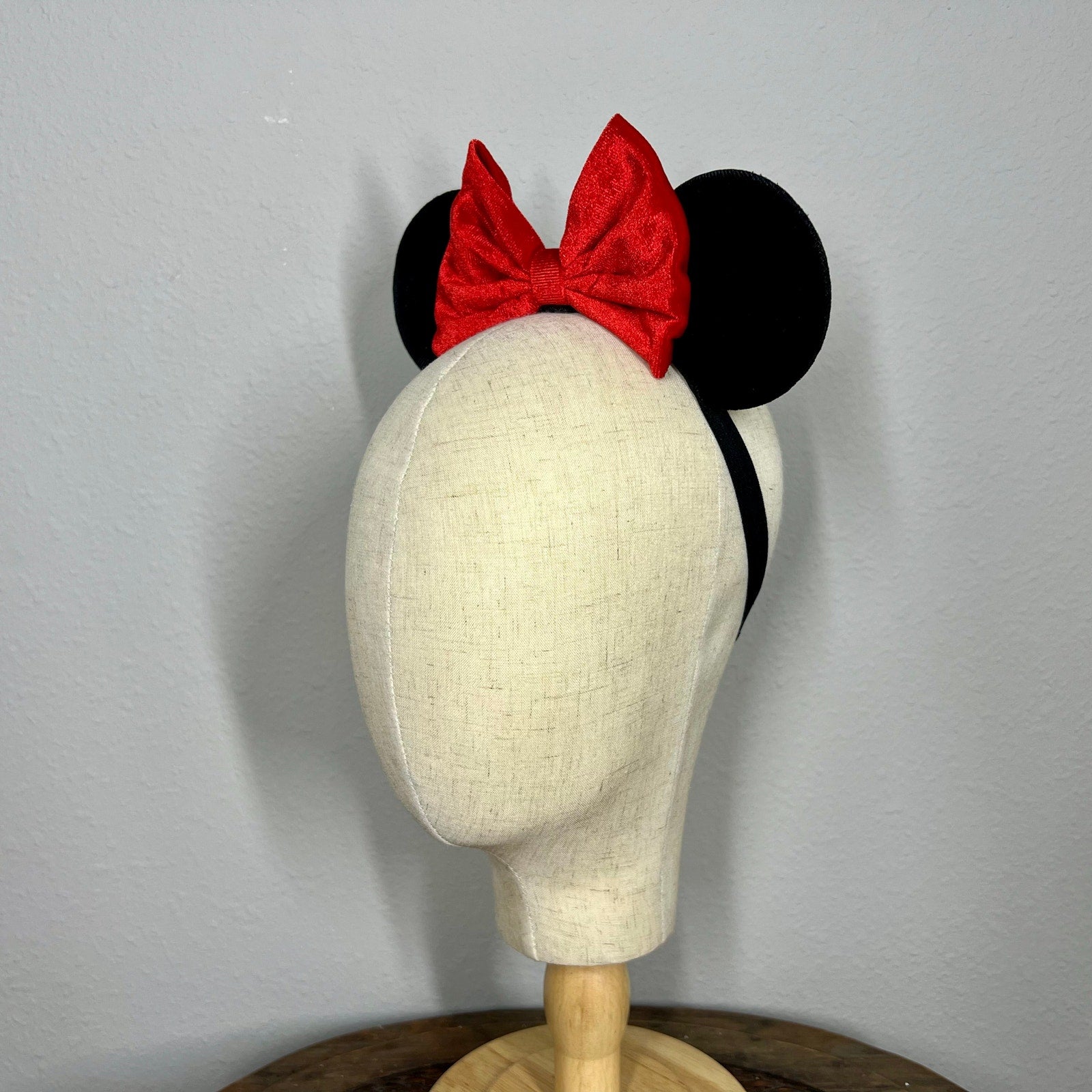 Mannequin head wearing black mouse ears with a red bow on a gray background