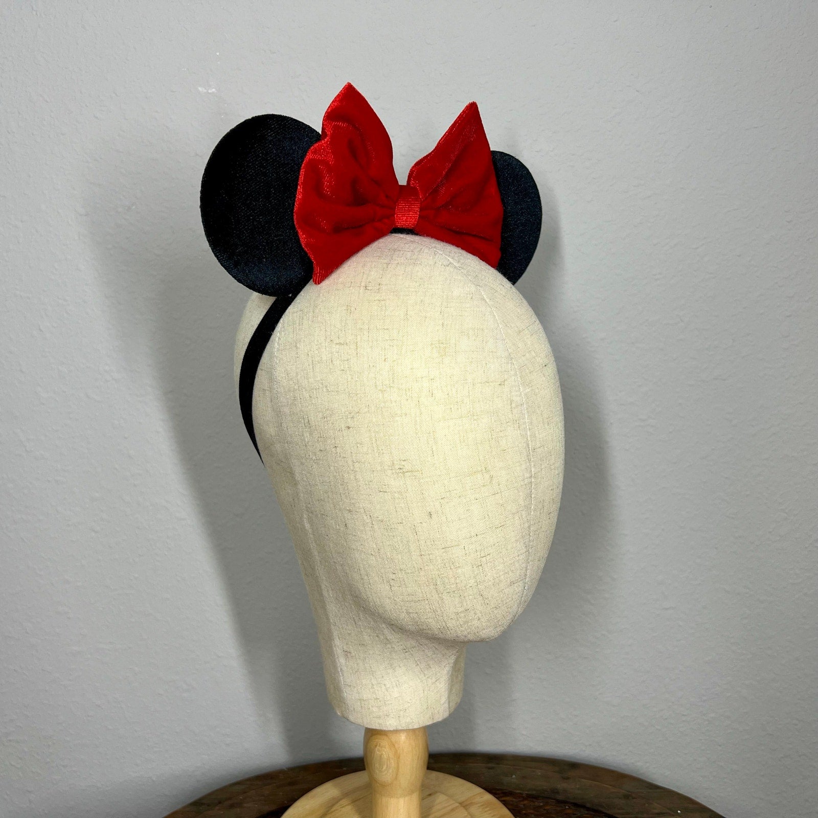 Black mouse ears with a red bow on a mannequin head against a gray background