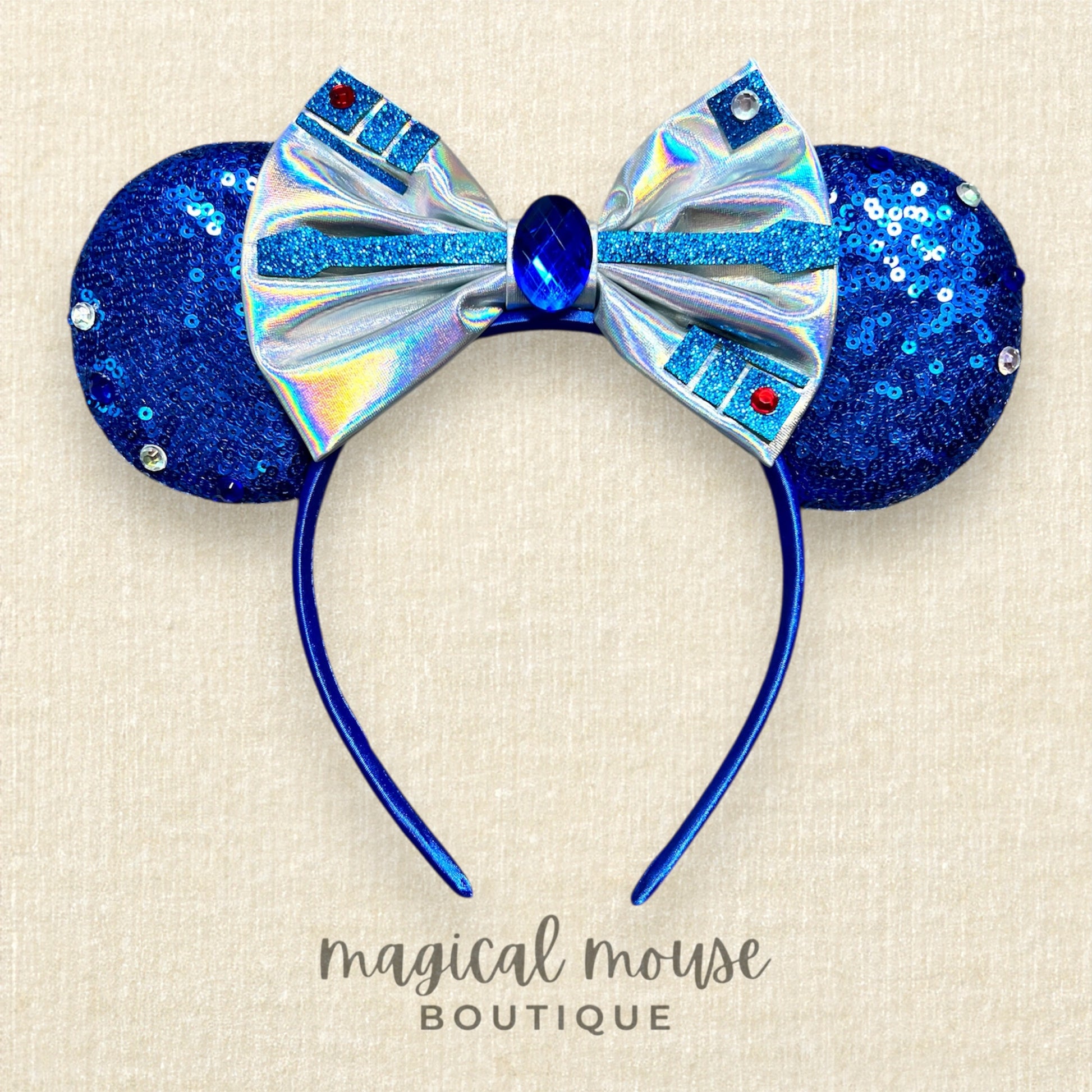 Blue and silver Minnie Mouse ears with a bow on a beige background, branded 'Magical Mouse Boutique'.