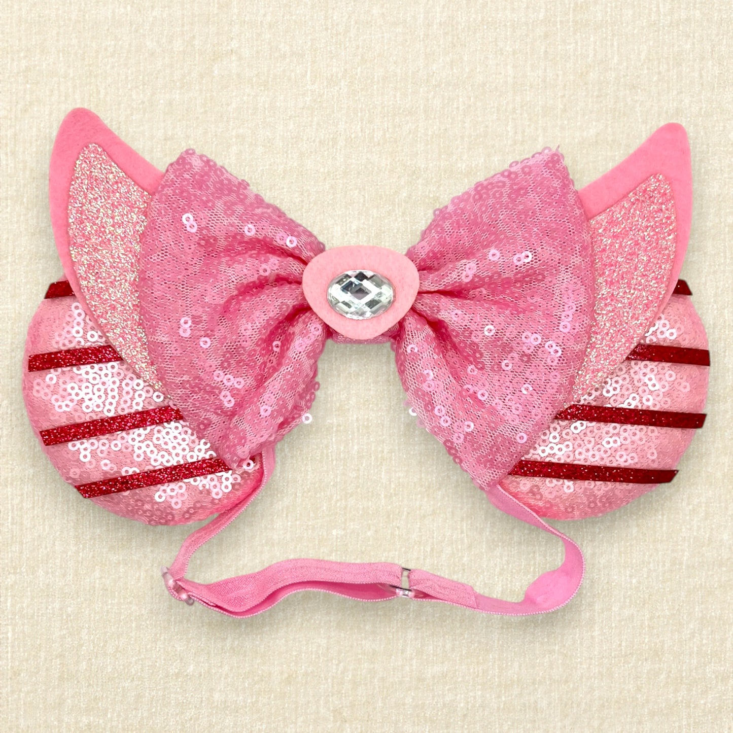 Pink sequin mouse ears with dark pink glitter stripes, pink sequin bow, and glitter piglet ears and nose detail on an elastic headband