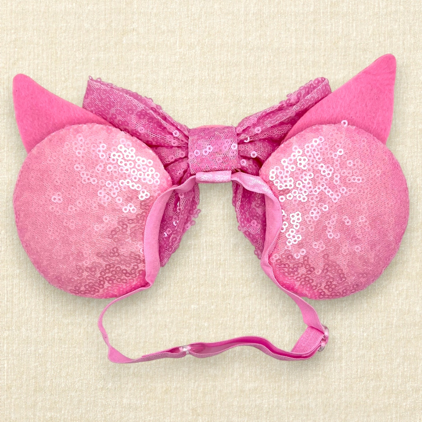 Pink sequin mouse ears with dark pink glitter stripes, pink sequin bow, and glitter piglet ears and nose detail on an elastic headband (back view)