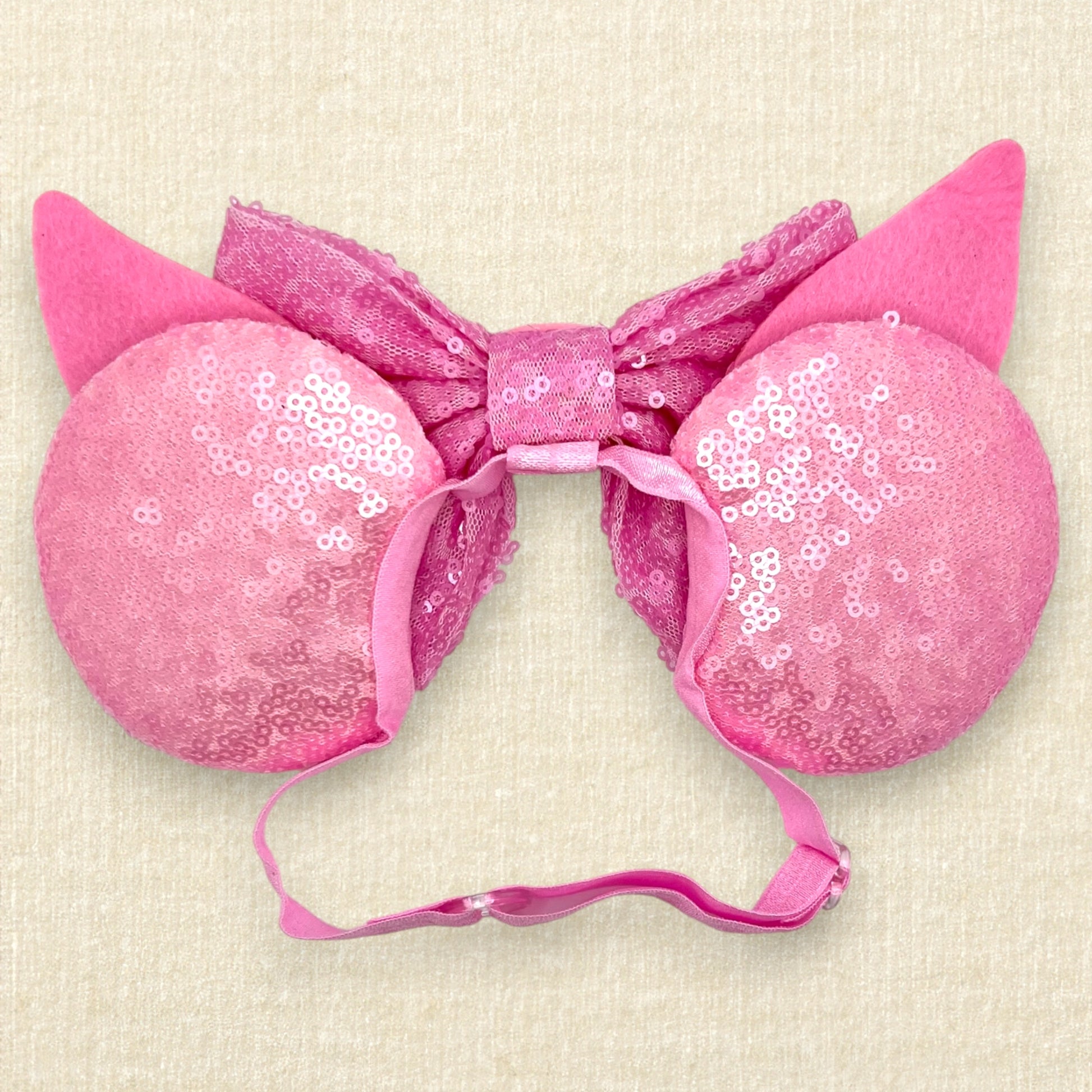 Pink sequin mouse ears with dark pink glitter stripes, pink sequin bow, and glitter piglet ears and nose detail on an elastic headband (back view)