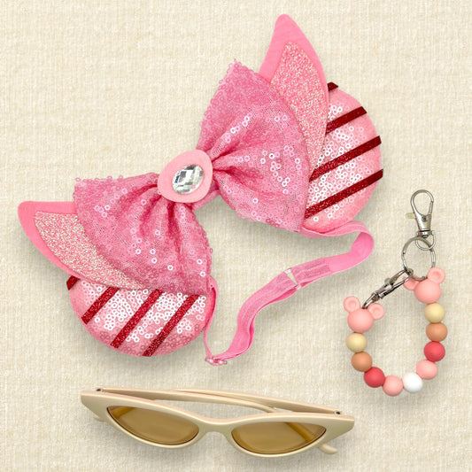 Pink sequin mouse ears with dark pink glitter stripes, pink sequin bow, and glitter piglet ears and nose detail on an elastic headband; cream cat-eye sunglasses; pink beaded mouse ears holder keychain