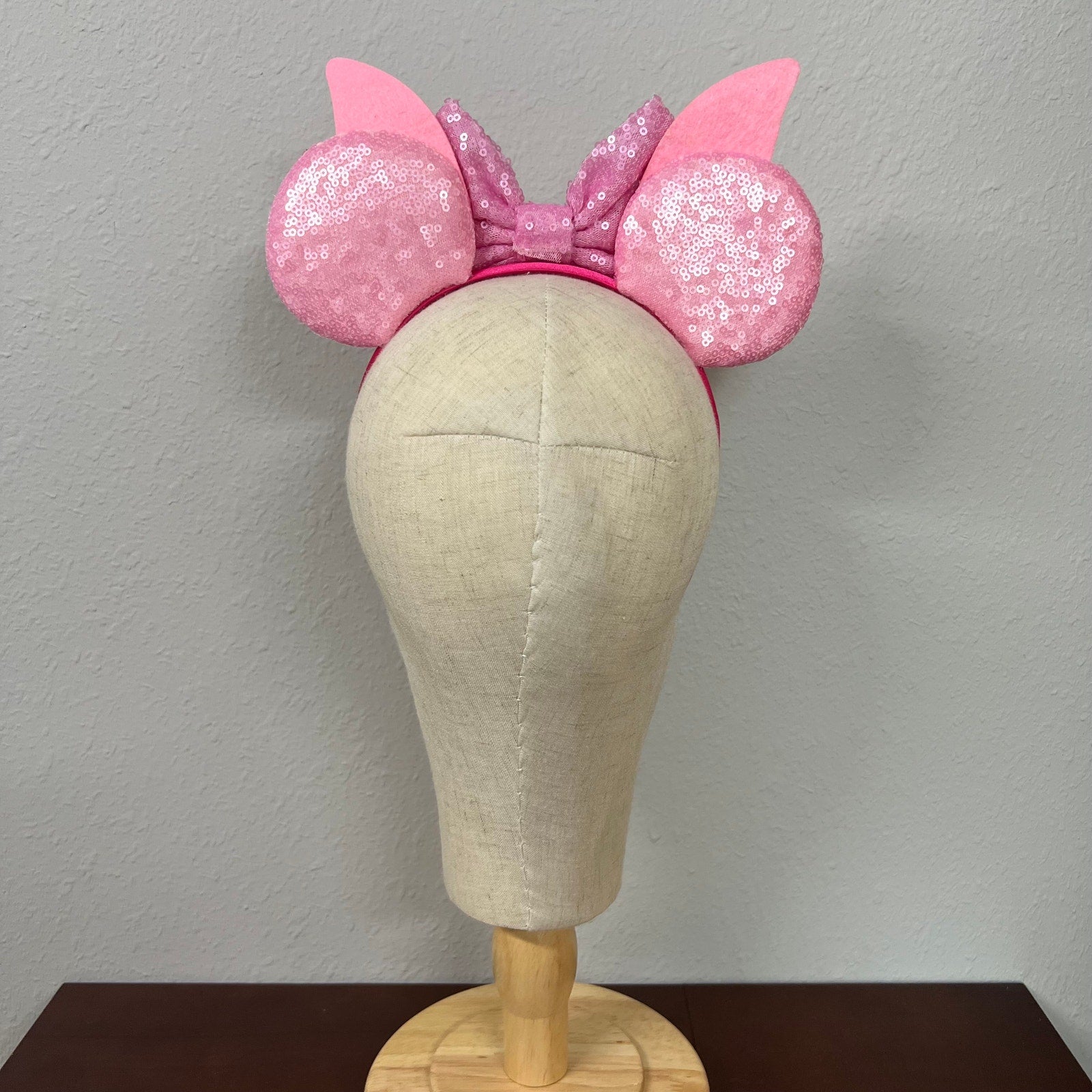 Pink mouse ears bow headband with striped sides on a mannequin head against a plain background