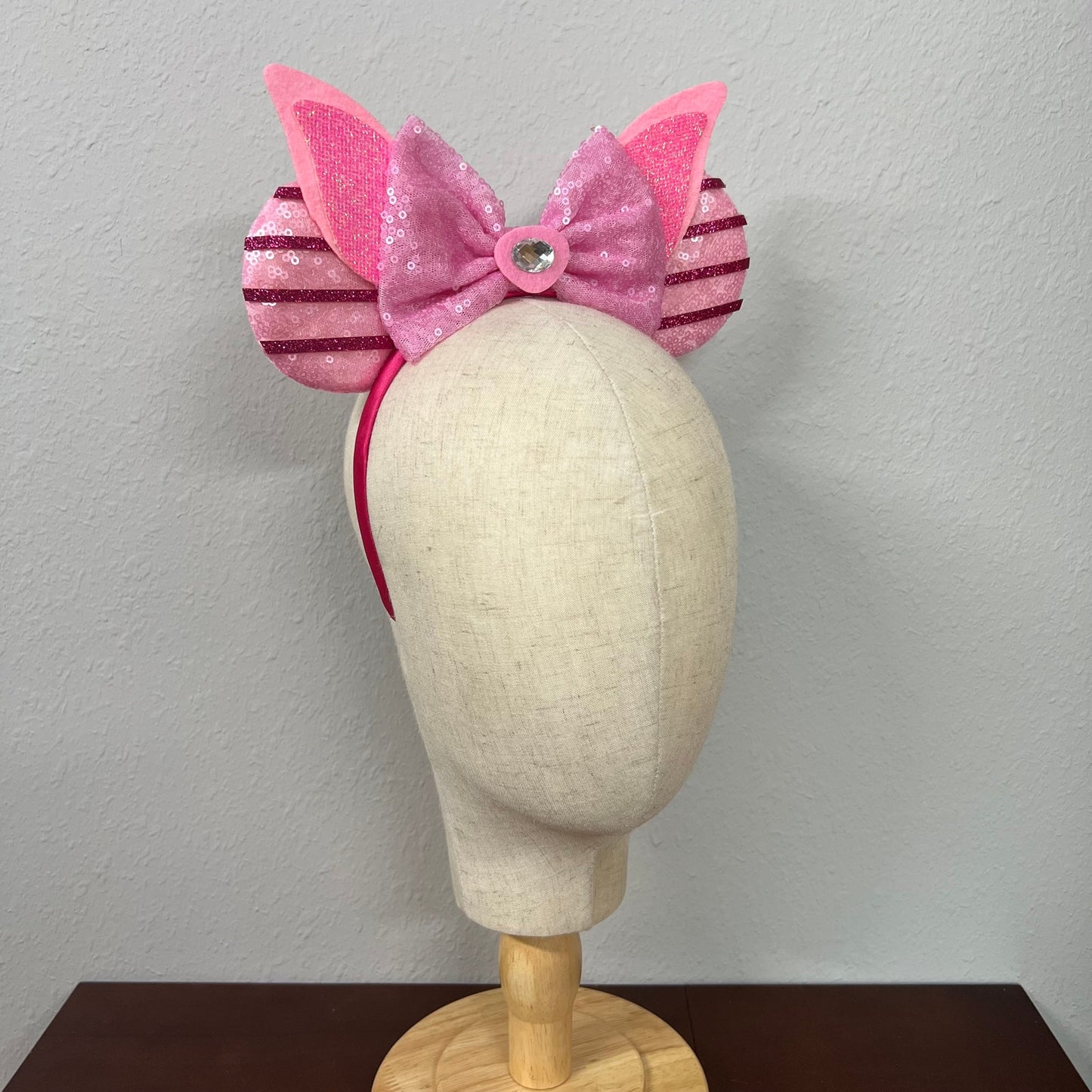 Pink mouse ears bow headband with striped sides on a mannequin head against a plain background