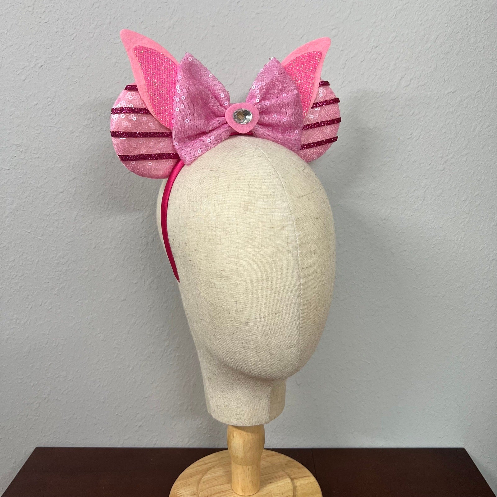 Pink mouse ears bow headband with striped sides on a mannequin head against a plain background