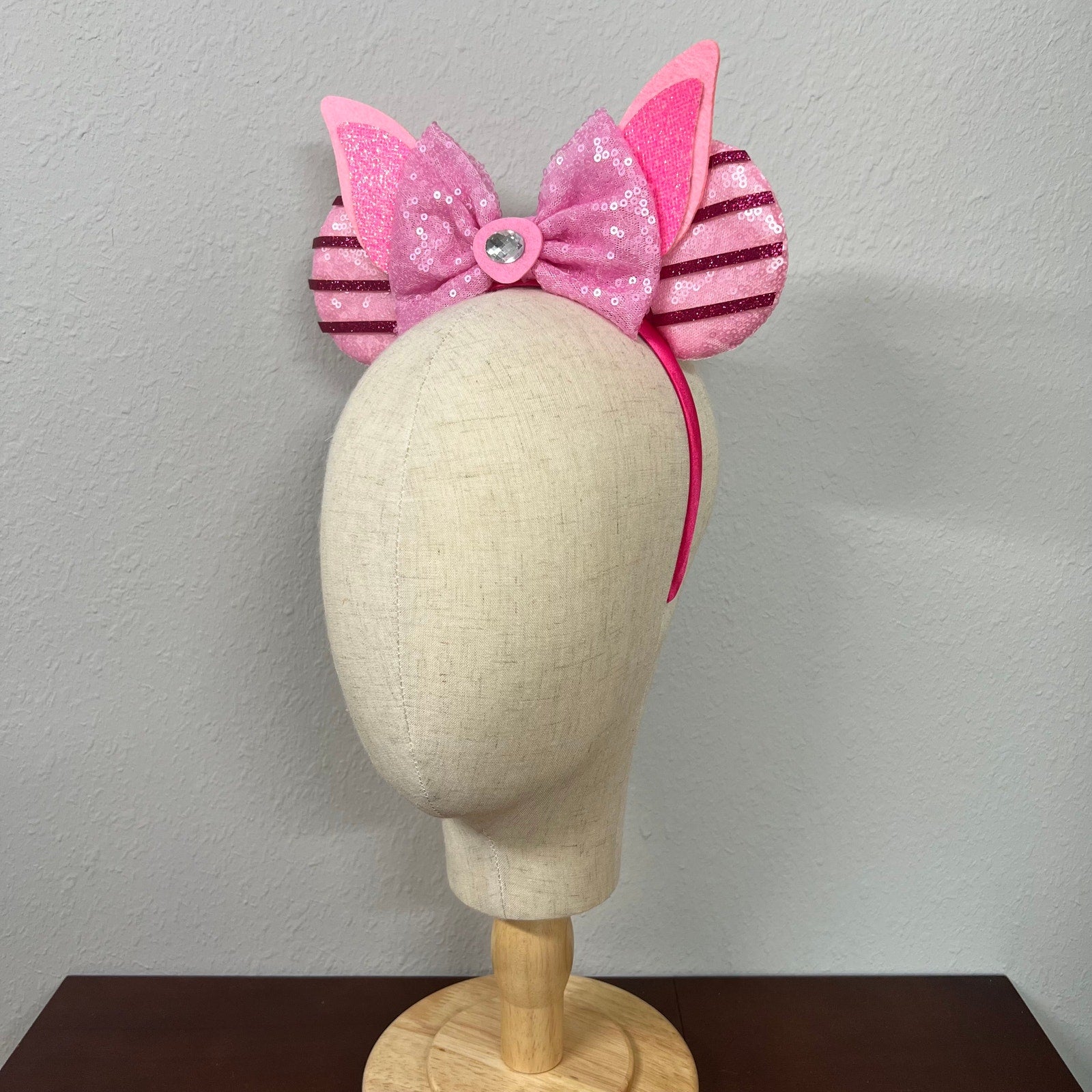 Pink mouse ears bow headband with striped sides on a mannequin head against a plain background