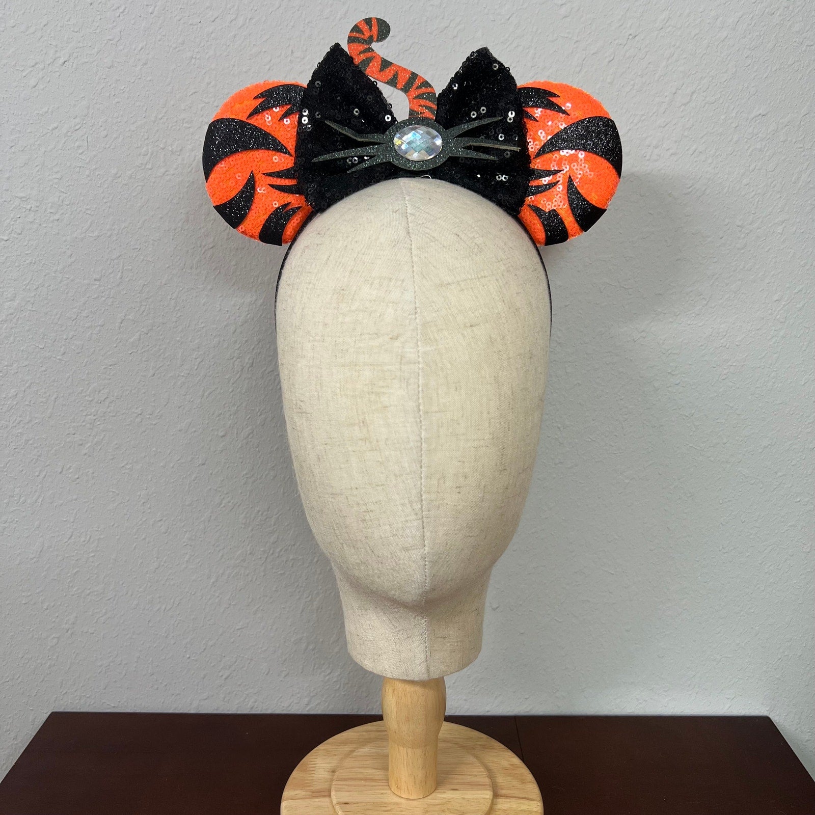 Orange mouse ears with black sequin bow, with black tiger stripes, black glitter whiskers, rhinestone nose, and orange and black tiger tail centerpiece on a mannequin head