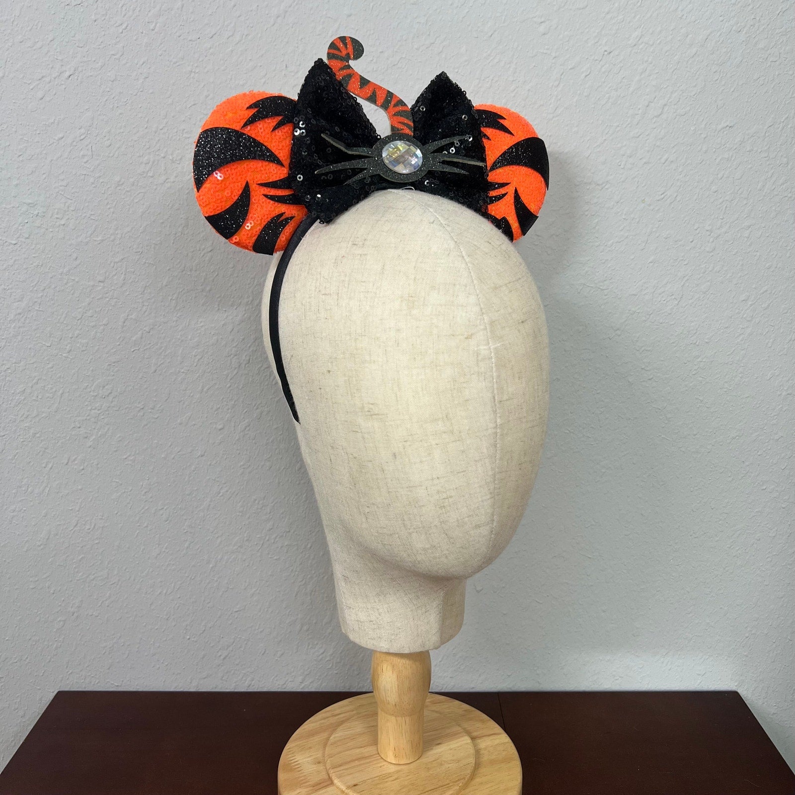 Orange mouse ears with black sequin bow, with black tiger stripes, black glitter whiskers, rhinestone nose, and orange and black tiger tail centerpiece on a mannequin head