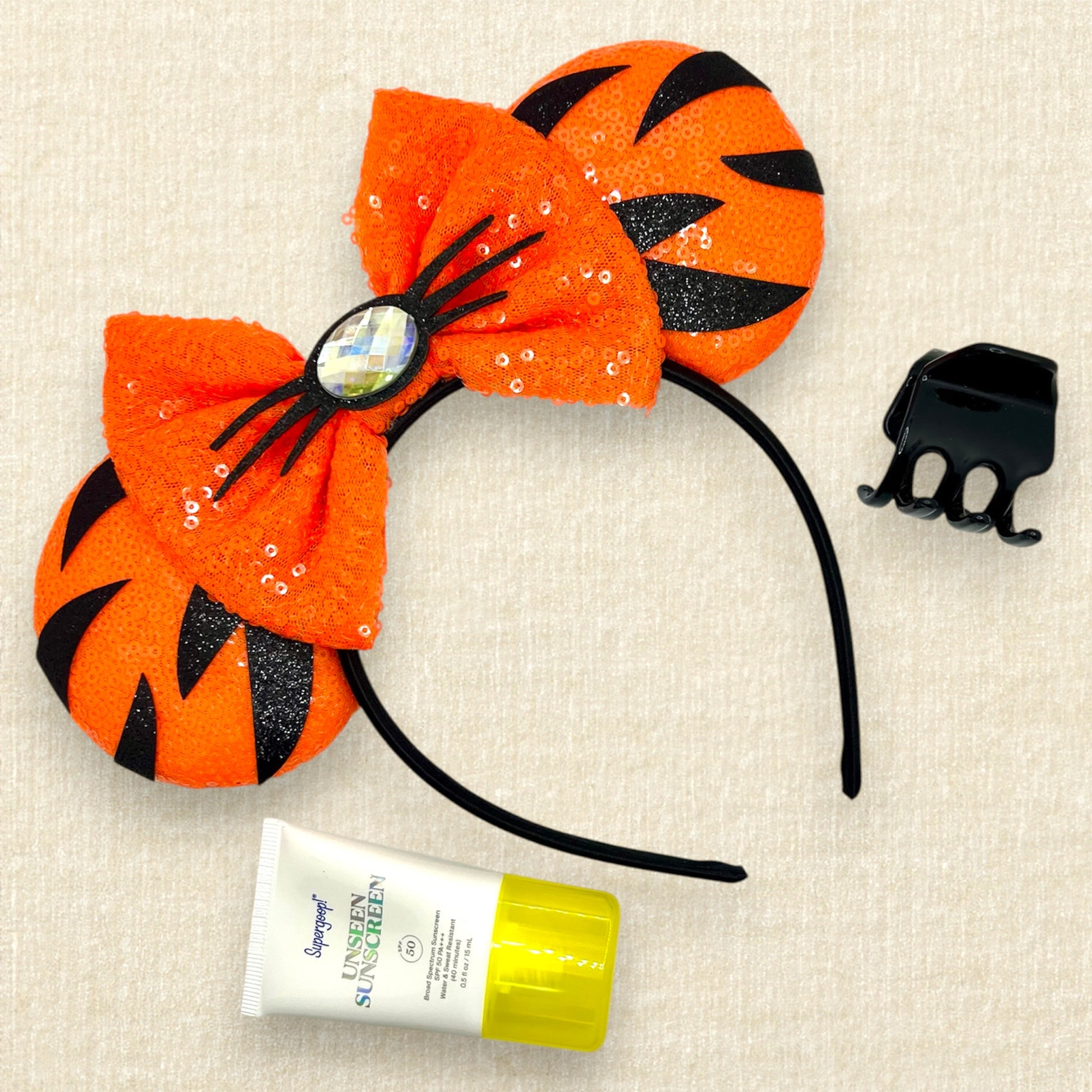 Orange sequin mouse ears headband with matching bow, black glitter tiger stripes, and rhinestone nose with black glitter whiskers; tube of sunscreen; black claw clip