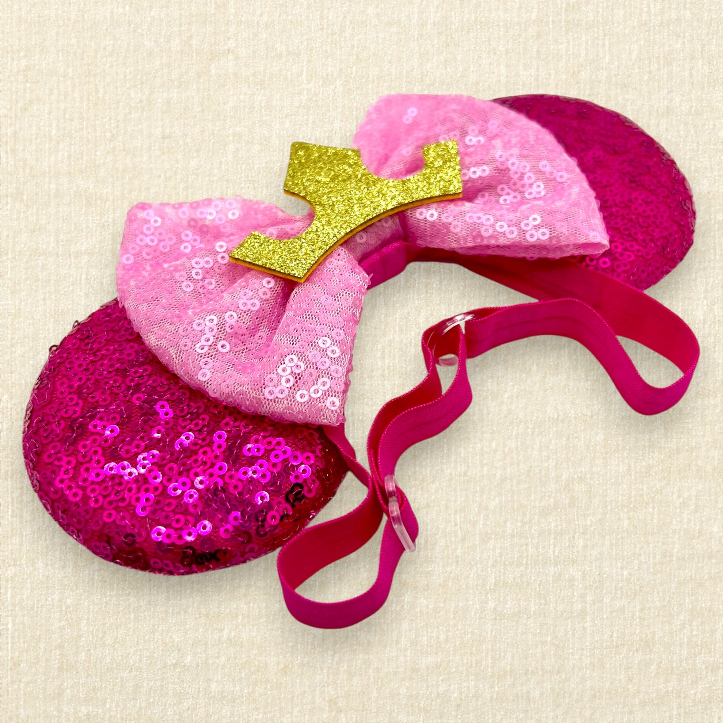 Hot pink sequin mouse ears with light pink sequin bow and gold crown on an elastic headband