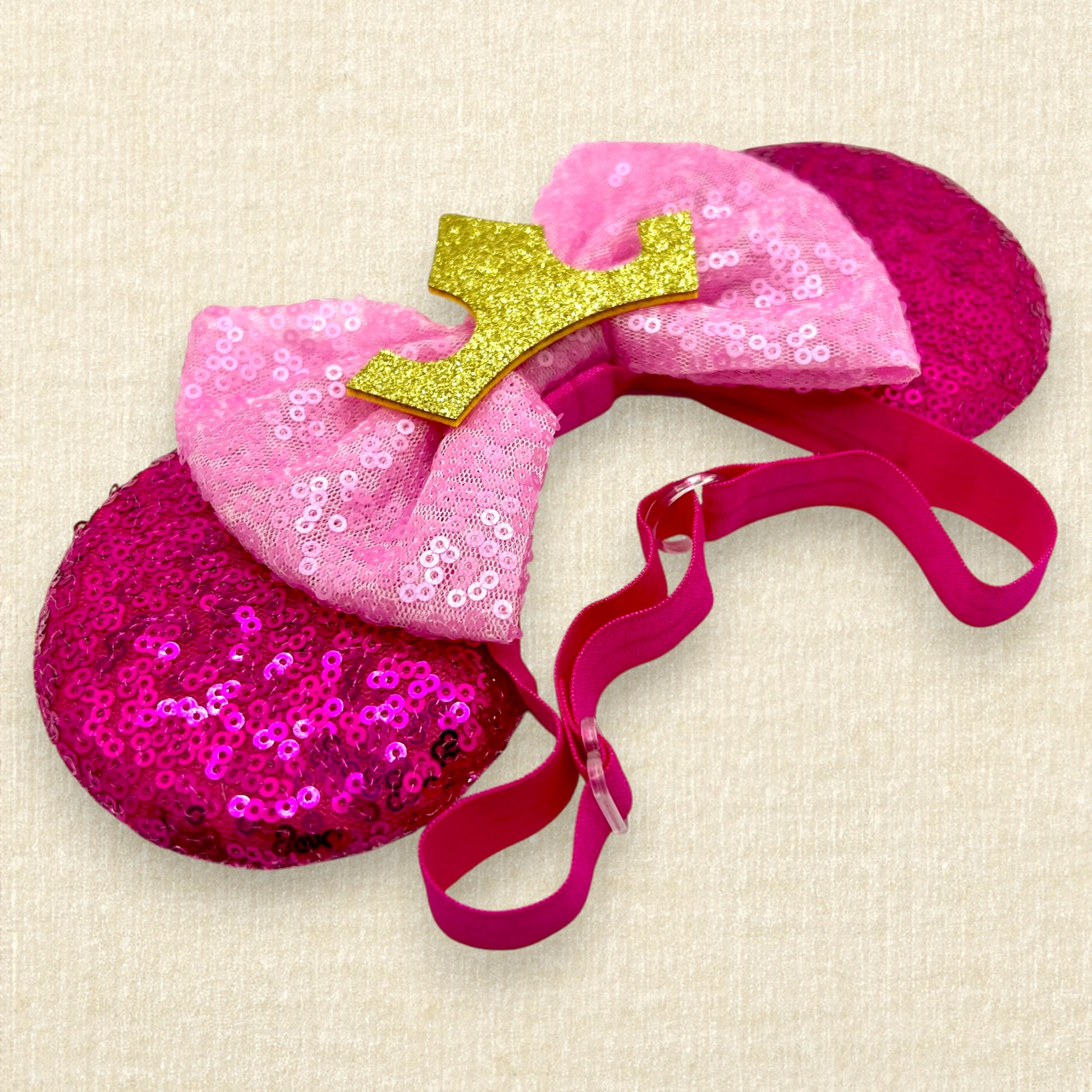 Hot pink sequin mouse ears with light pink sequin bow and gold crown on an elastic headband