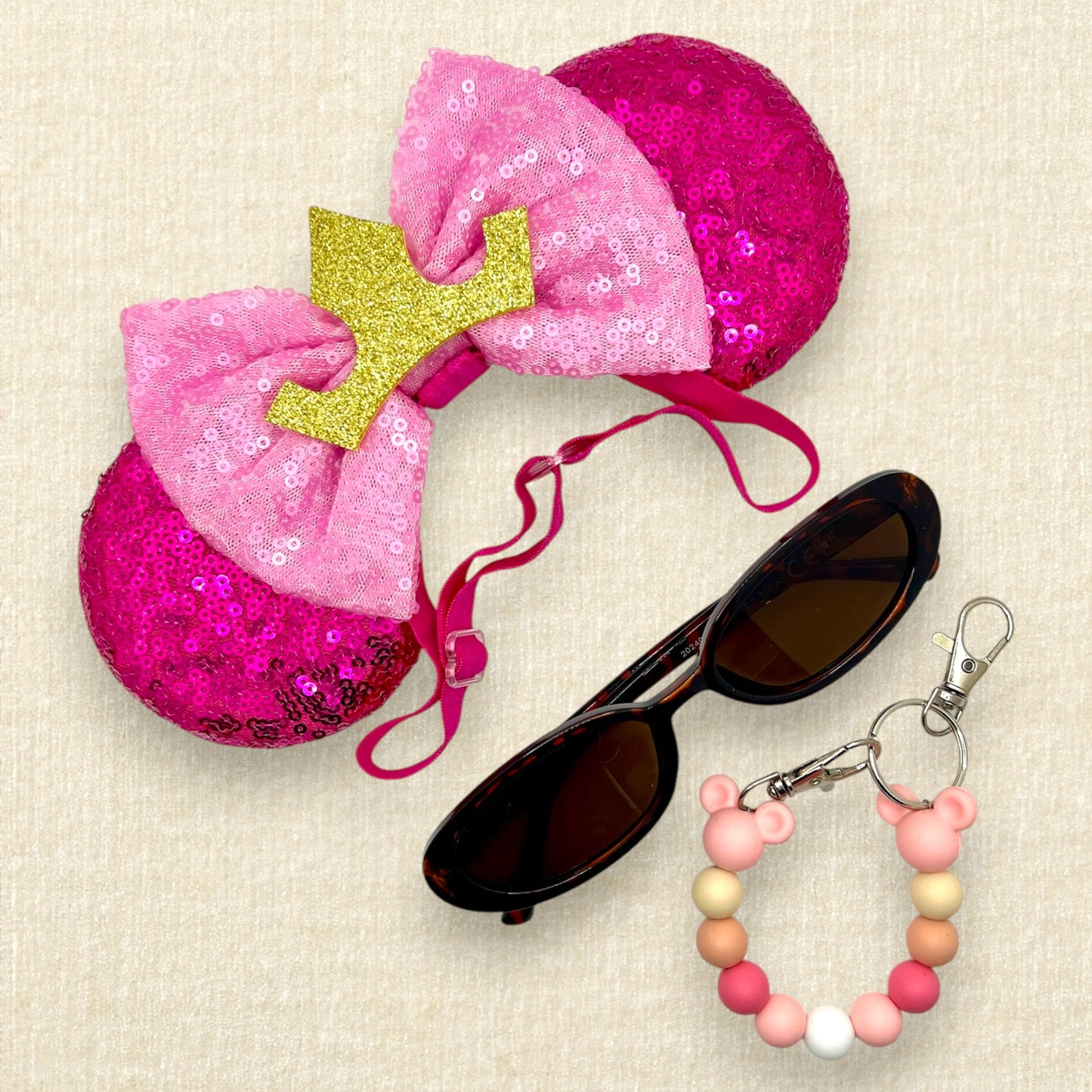 Hot pink sequin mouse ears with light pink sequin bow and gold crown on an elastic headband; tortoiseshell sunglasses; pink beaded mouse ears holder keychain
