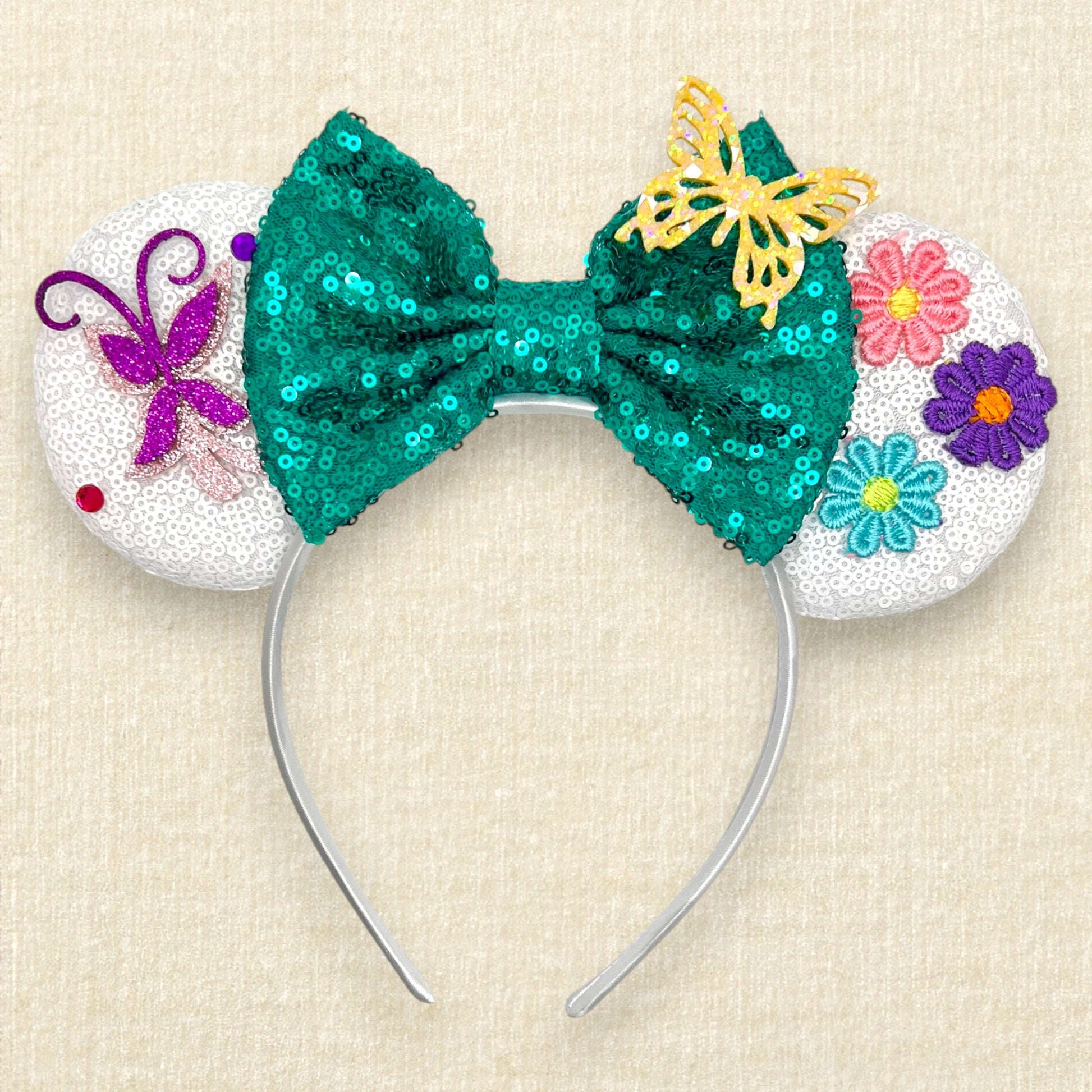 White sequin mouse ears with butterflies and flower details and a green sequin bow