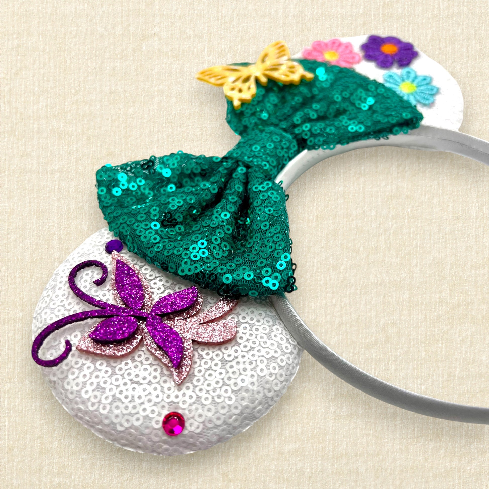 White sequin mouse ears with butterflies and flower details and a green sequin bow