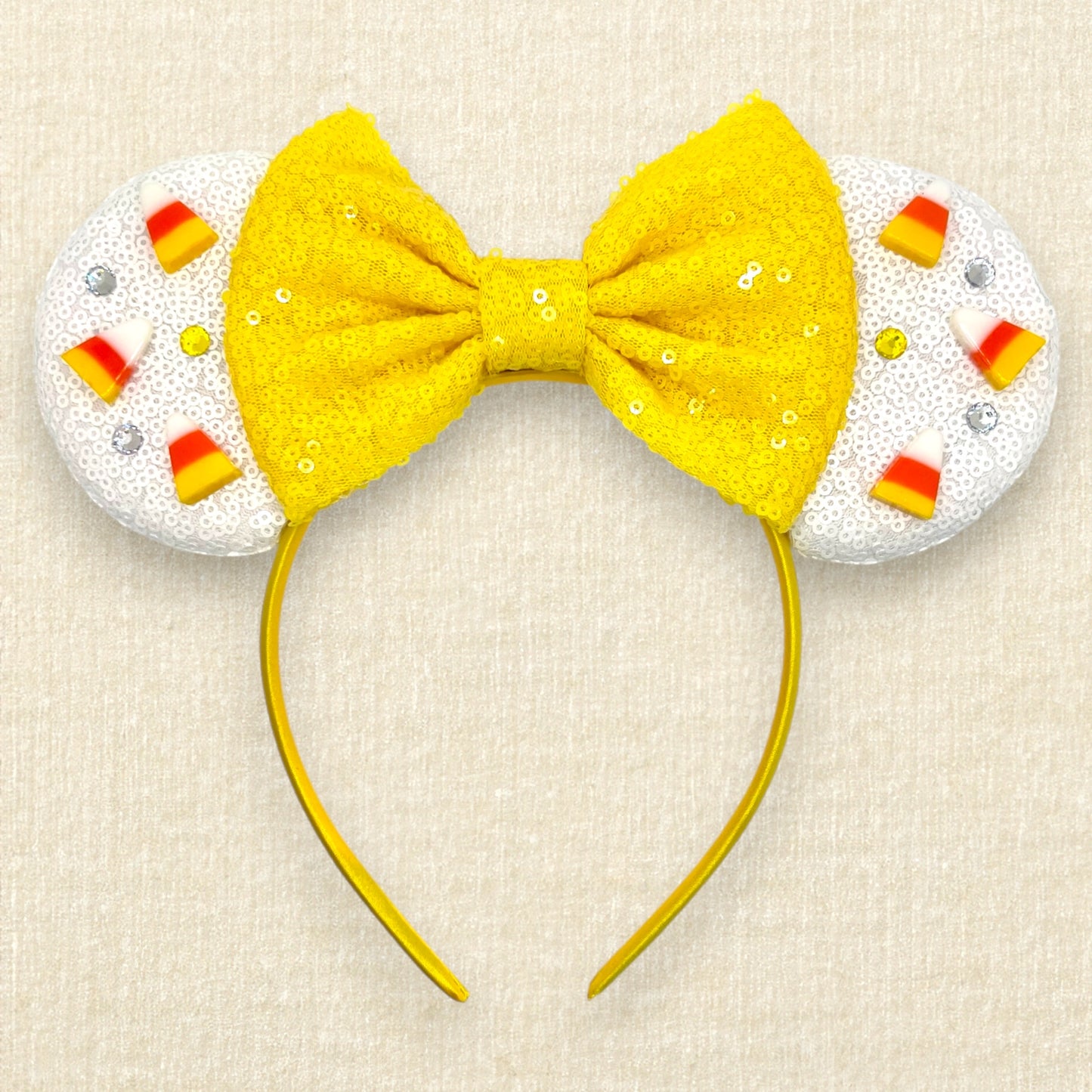 Halloween-themed mouse ears headband with white ears, candy corn pieces, rhinestones, and a yellow bow