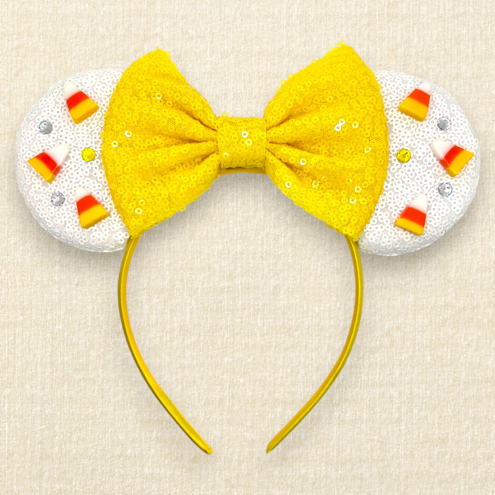 Halloween-themed mouse ears headband with white ears, candy corn pieces, rhinestones, and a yellow bow