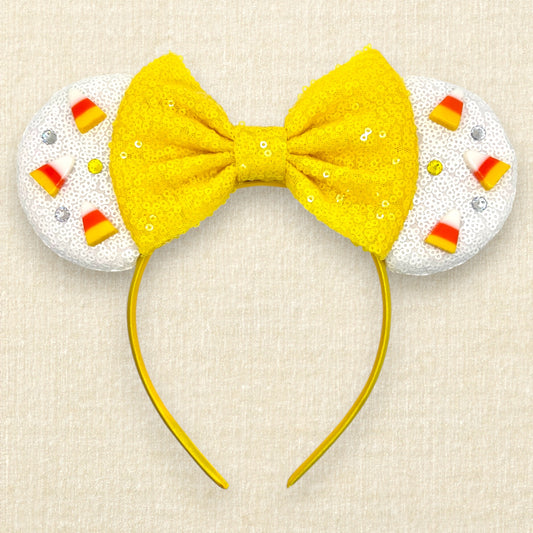 Halloween-themed mouse ears headband with white ears, candy corn pieces, rhinestones, and a yellow bow